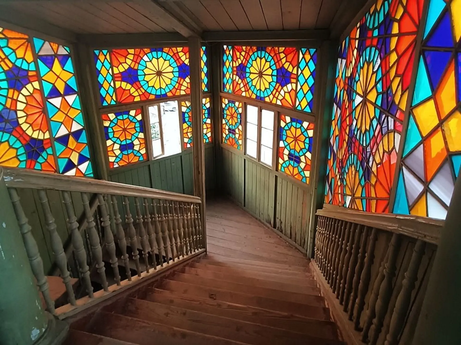 Colorful stained glass windows illuminate a wooden staircase in Tbilisi, Georgia