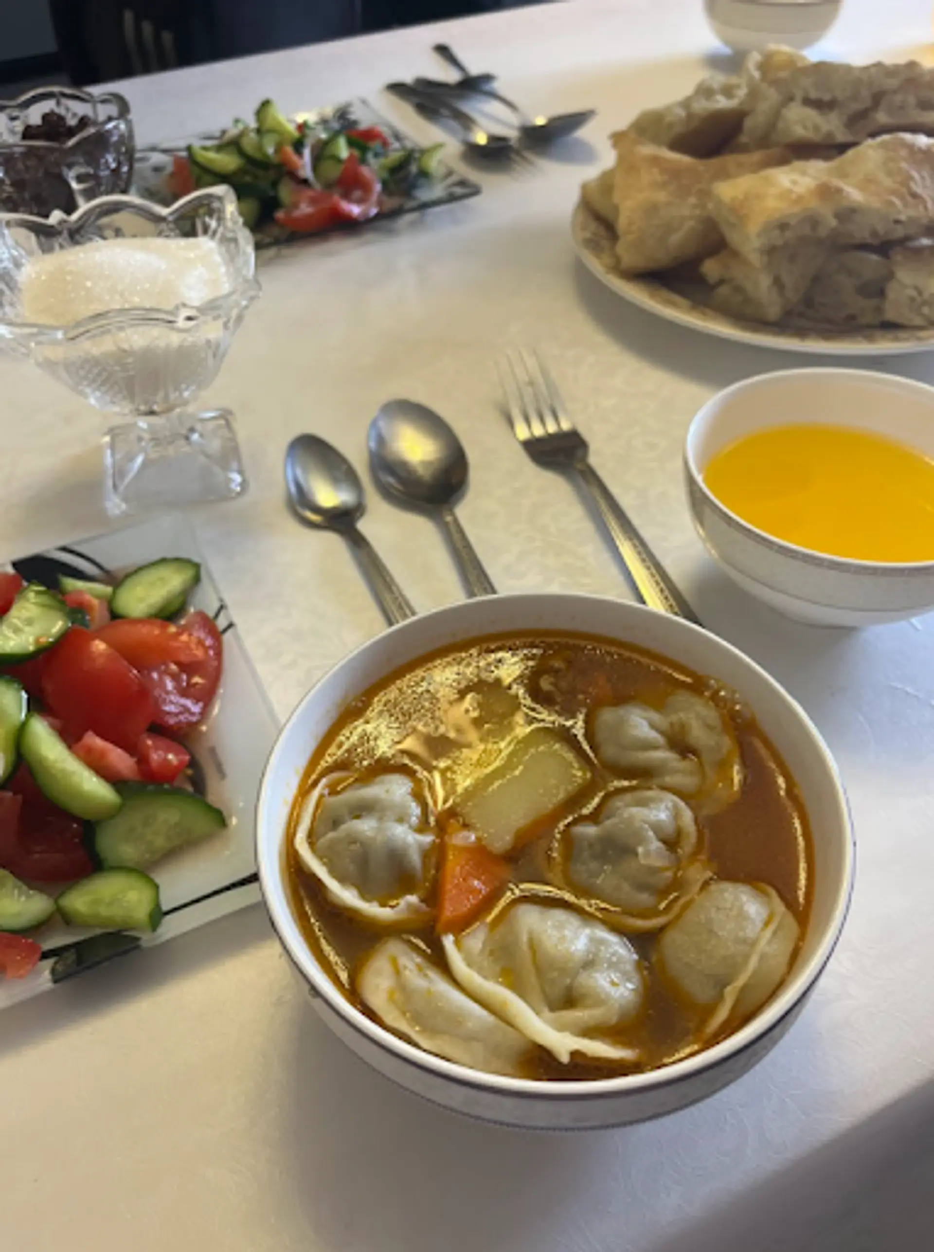 A dining table in Kyrgyzstan featuring a meal of traditional dumpling soup, fresh salad, and bread.