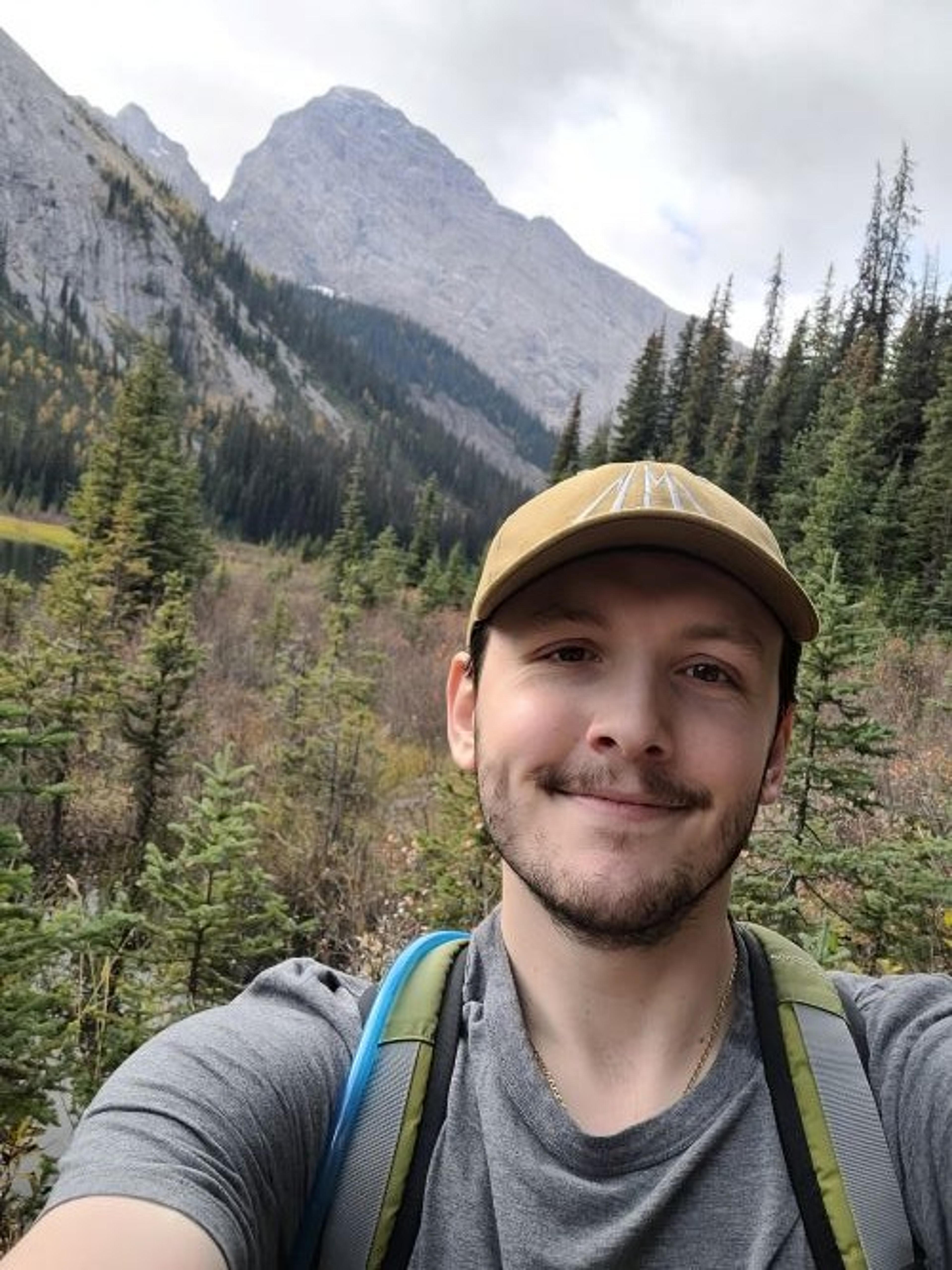 A person takes a selfie amidst the mountainous landscapes and dense forests of Kananaskis Country in Alberta.