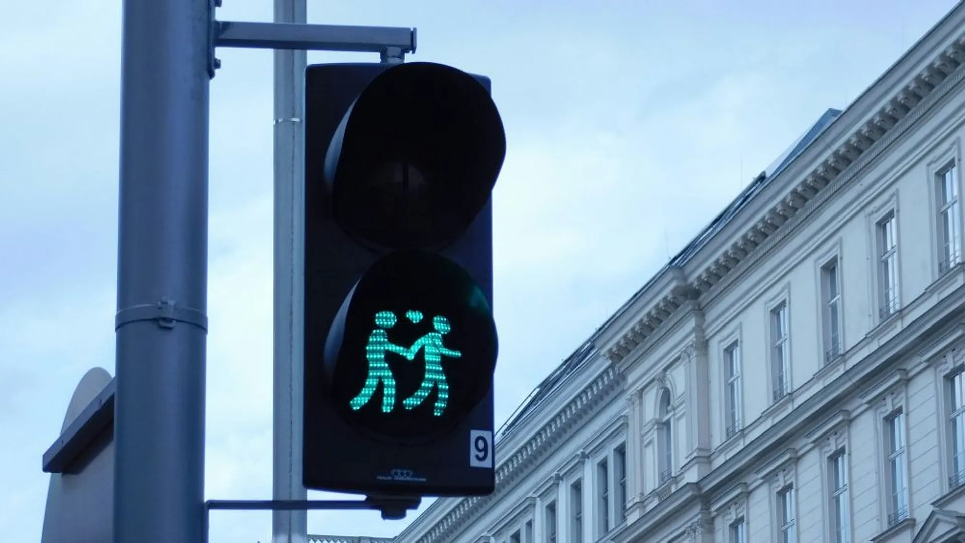 A unique traffic light in Vienna showcases a green pedestrian signal depicting two figures walking together.