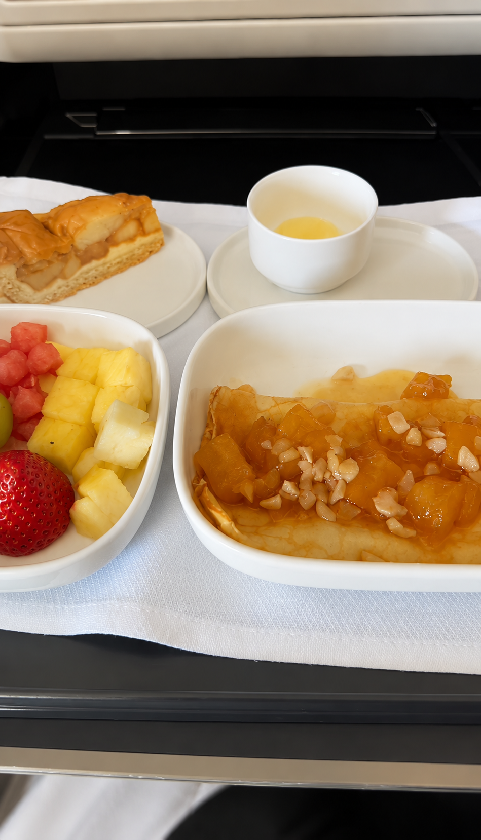 A gourmet meal featuring fruit and desserts is elegantly arranged on an airplane tray table.