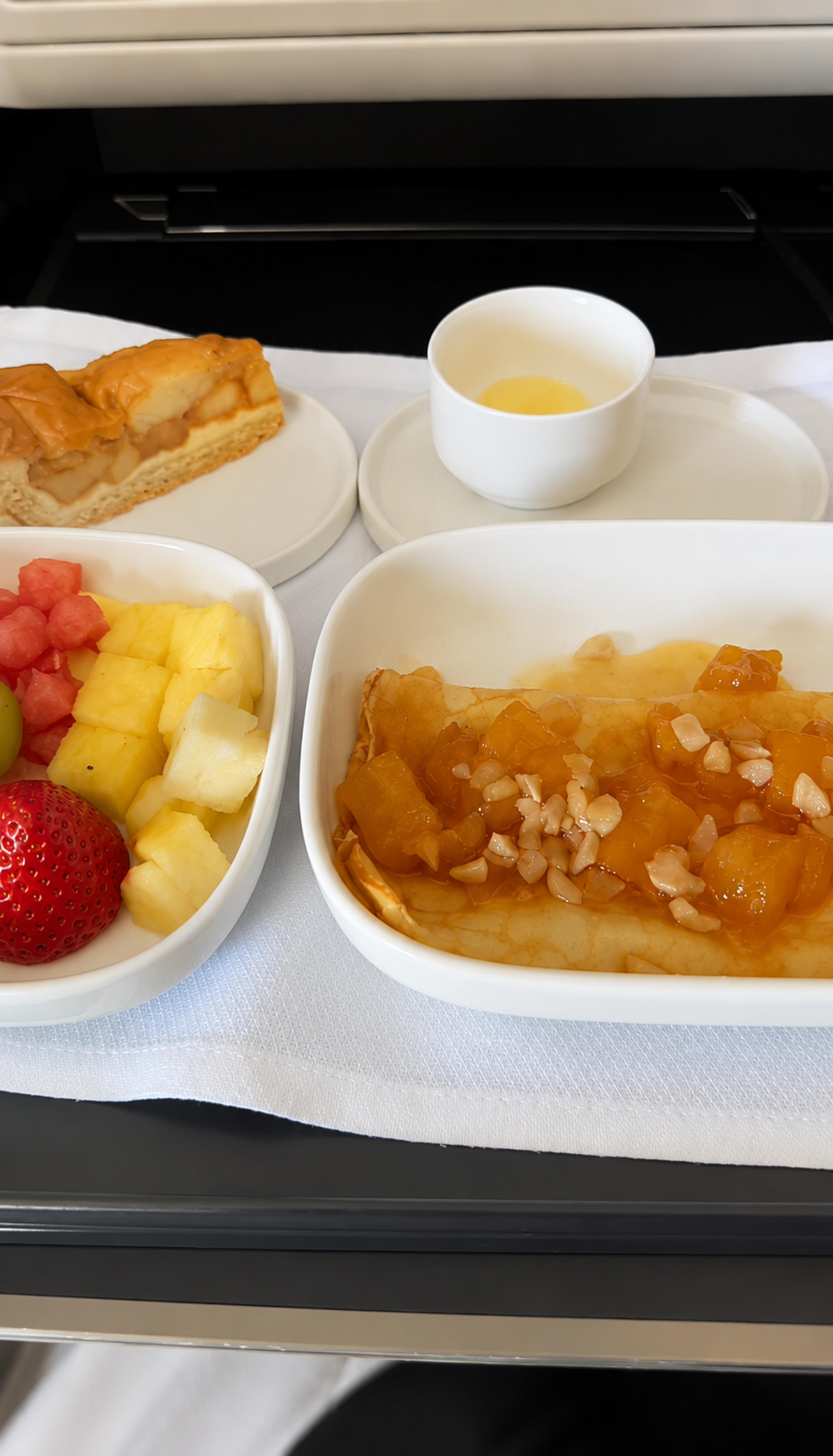 A gourmet meal featuring fruit and desserts is elegantly arranged on an airplane tray table.