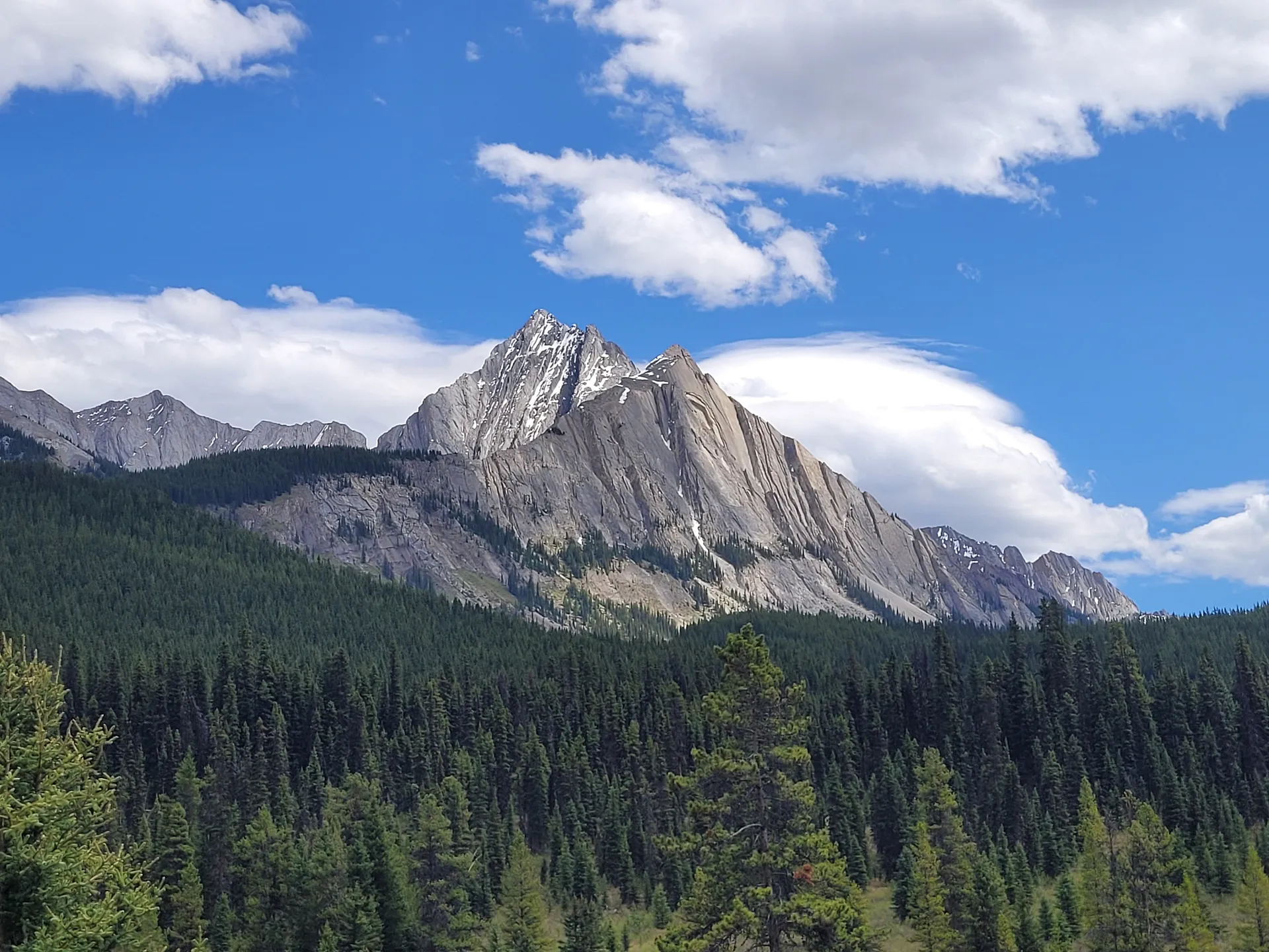 Majestic mountain peaks rise over a dense forest near Larry's Camp and the Ink Pots in Banff National Park, Alberta, Canada.