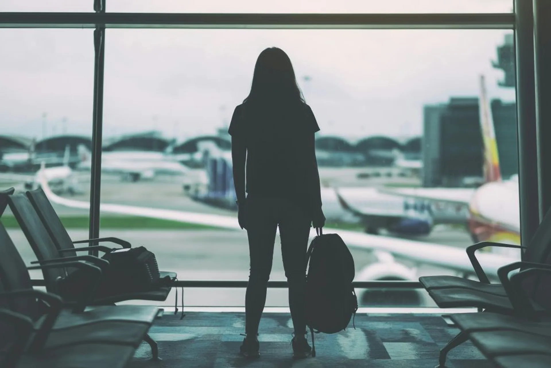 A person with luggage waits at a departure gate, overlooking the planes at Hong Kong International Airport.