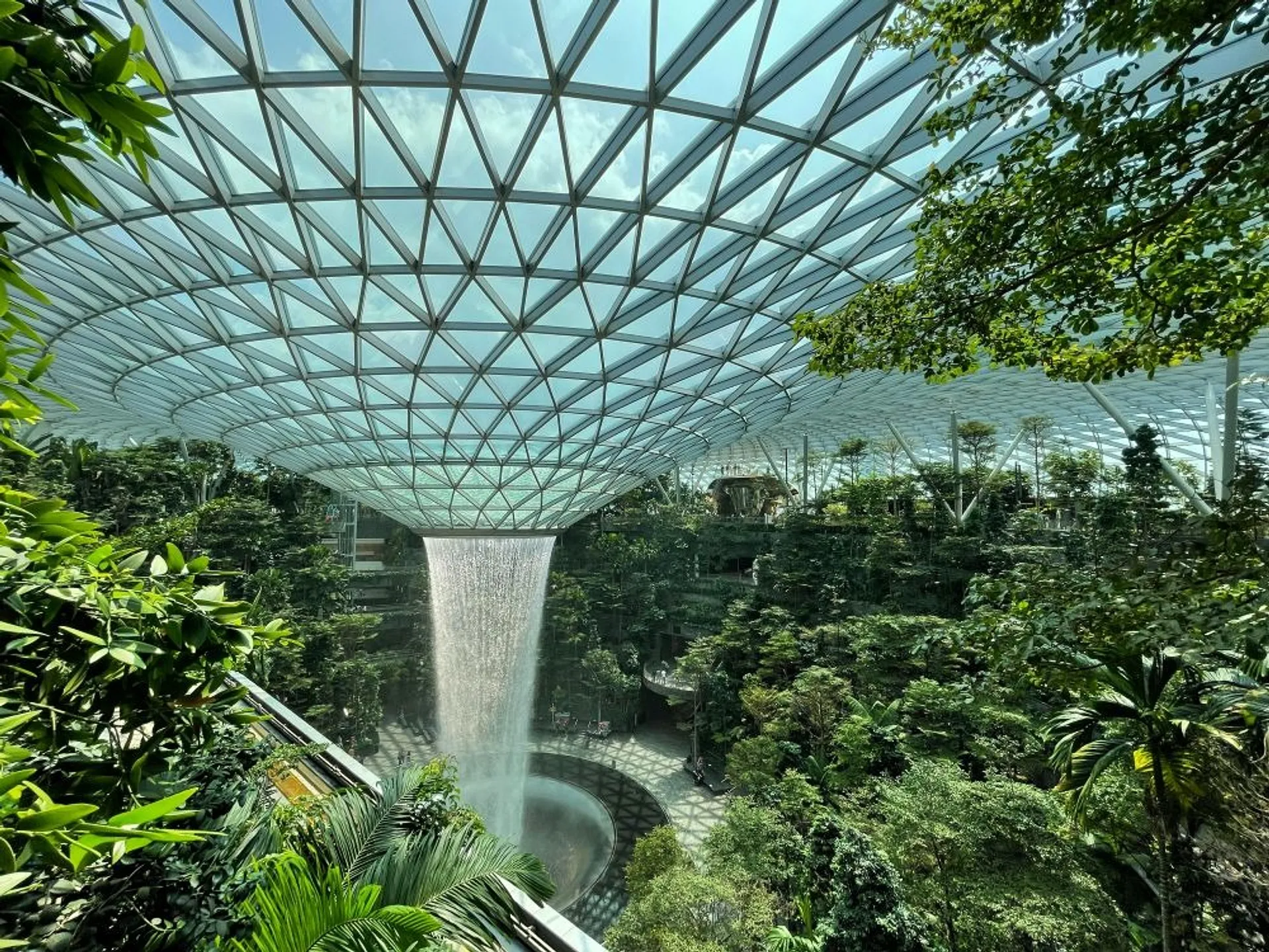 A spectacular indoor waterfall cascades from the roof of the Jewel Changi Airport in Singapore, surrounded by lush greenery.