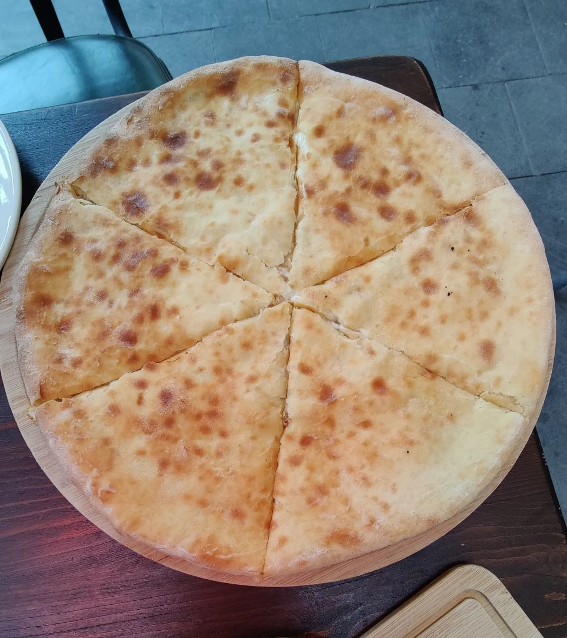 A freshly baked khachapuri, sliced into six pieces, rests on a wooden table in Tbilisi.