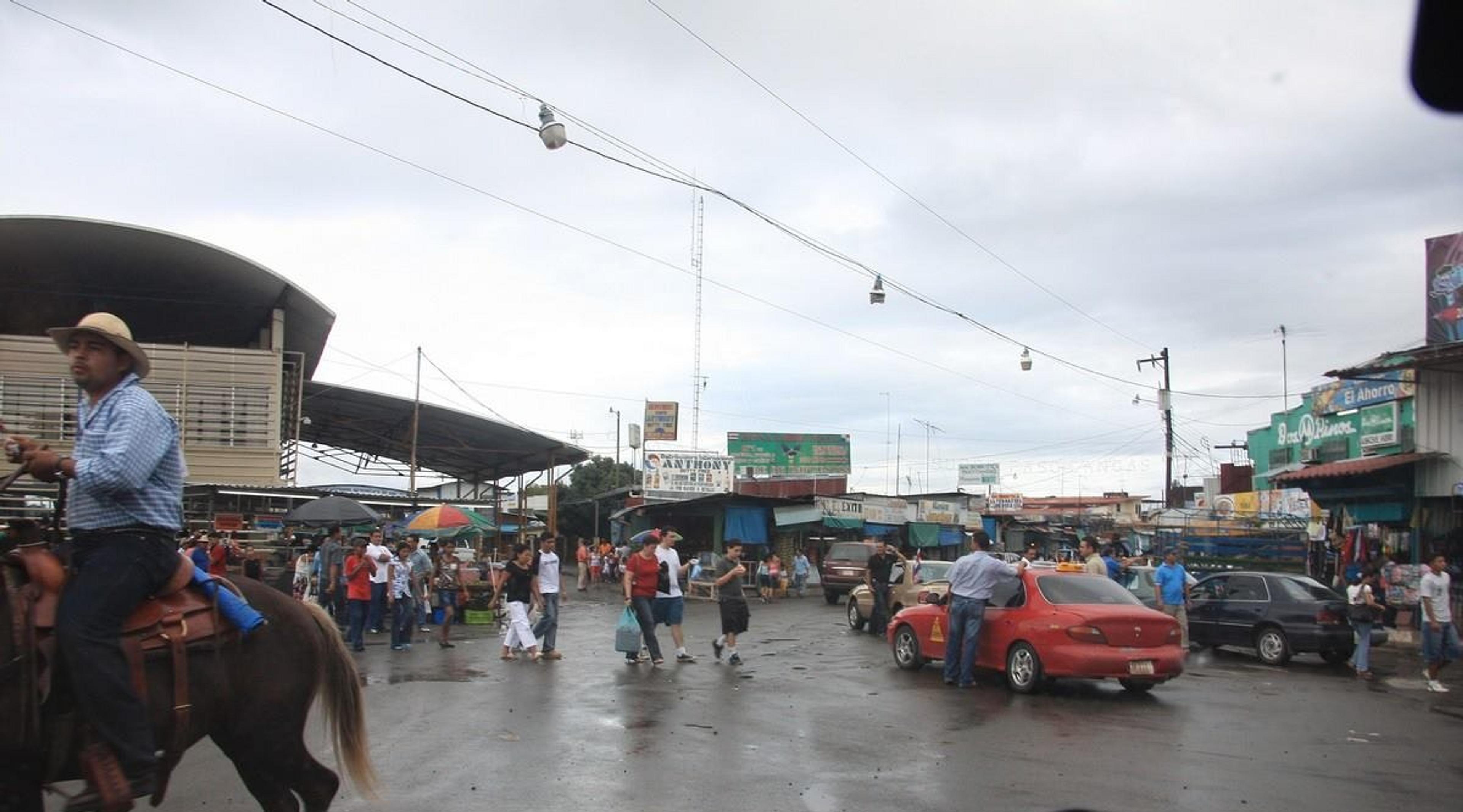A bustling street scene unfolds in the border town of Paso Canoas 
featuring a man on horseback and lively market activity.