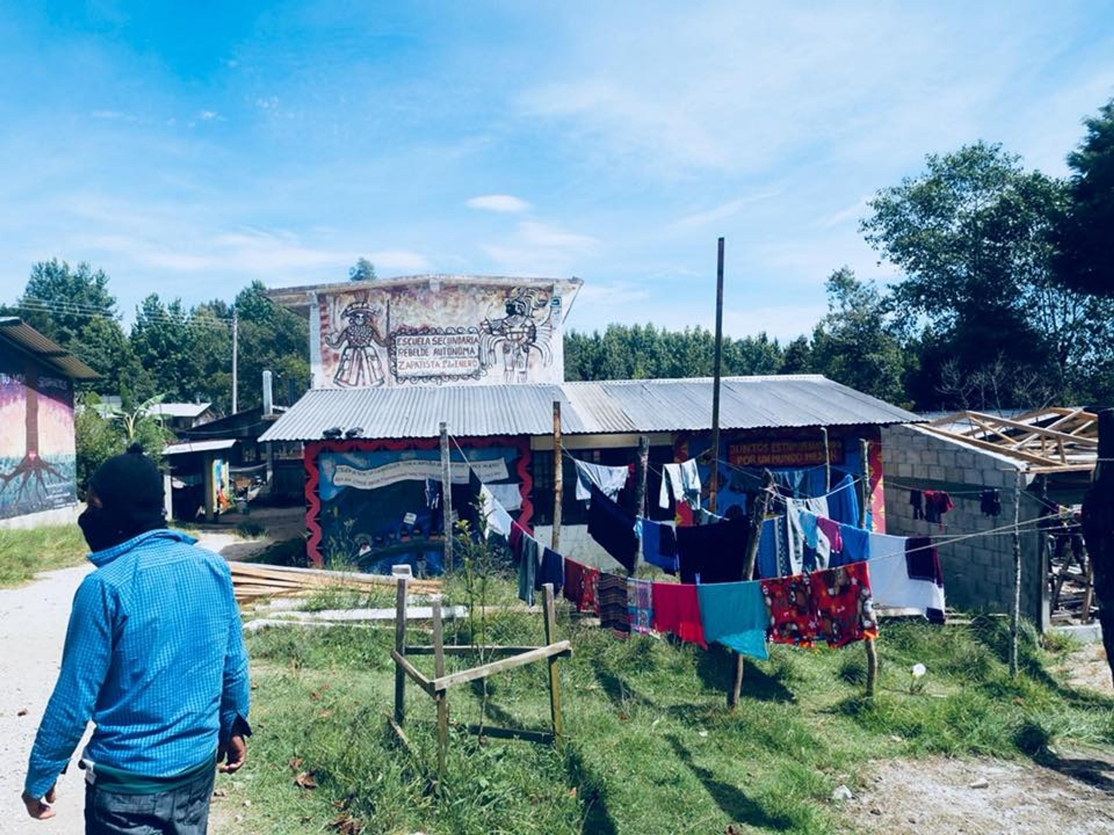 A rural scene in Chiapas, Mexico, featuring a building adorned with Zapatista murals and colorful clothes hanging on lines.