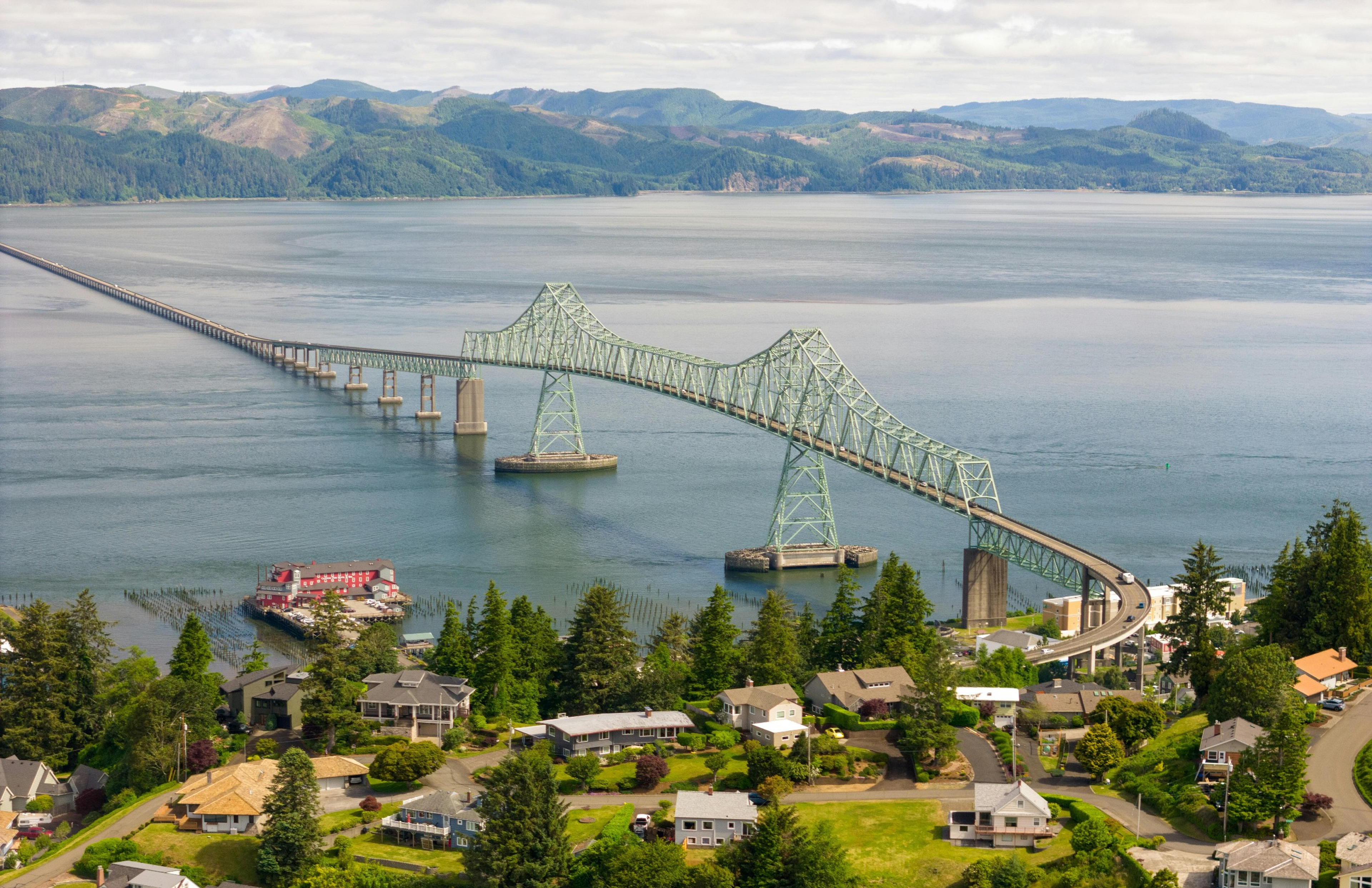 The Astoria-Megler Bridge spans across the Columbia River in Astoria, Oregon, connecting to Washington state amidst lush greenery and distant hills.