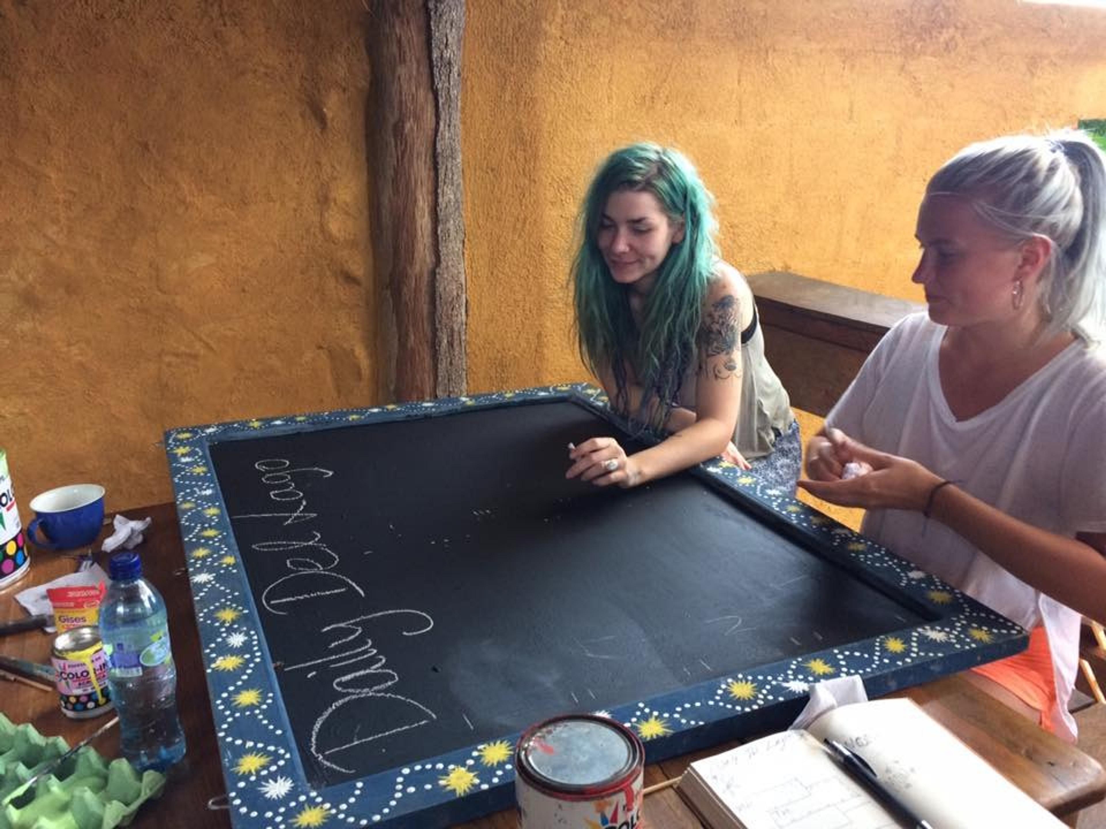 Two people engage in a creative chalkboard activity at a hostel.