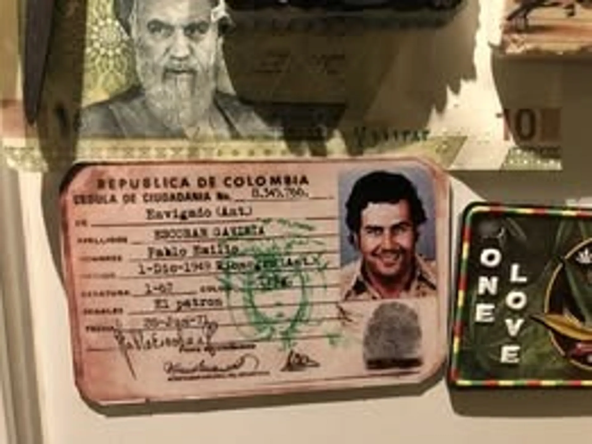 A display includes a novelty Colombian ID card featuring an individual named "Pablo Emilio Escobar" alongside eclectic items, possibly in a themed exhibit.
