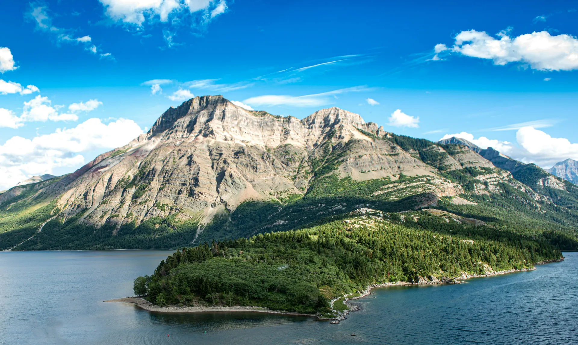 A serene view of Waterton Lakes National Park in Alberta, Canada, featuring a lush green peninsula and majestic mountain backdrop.