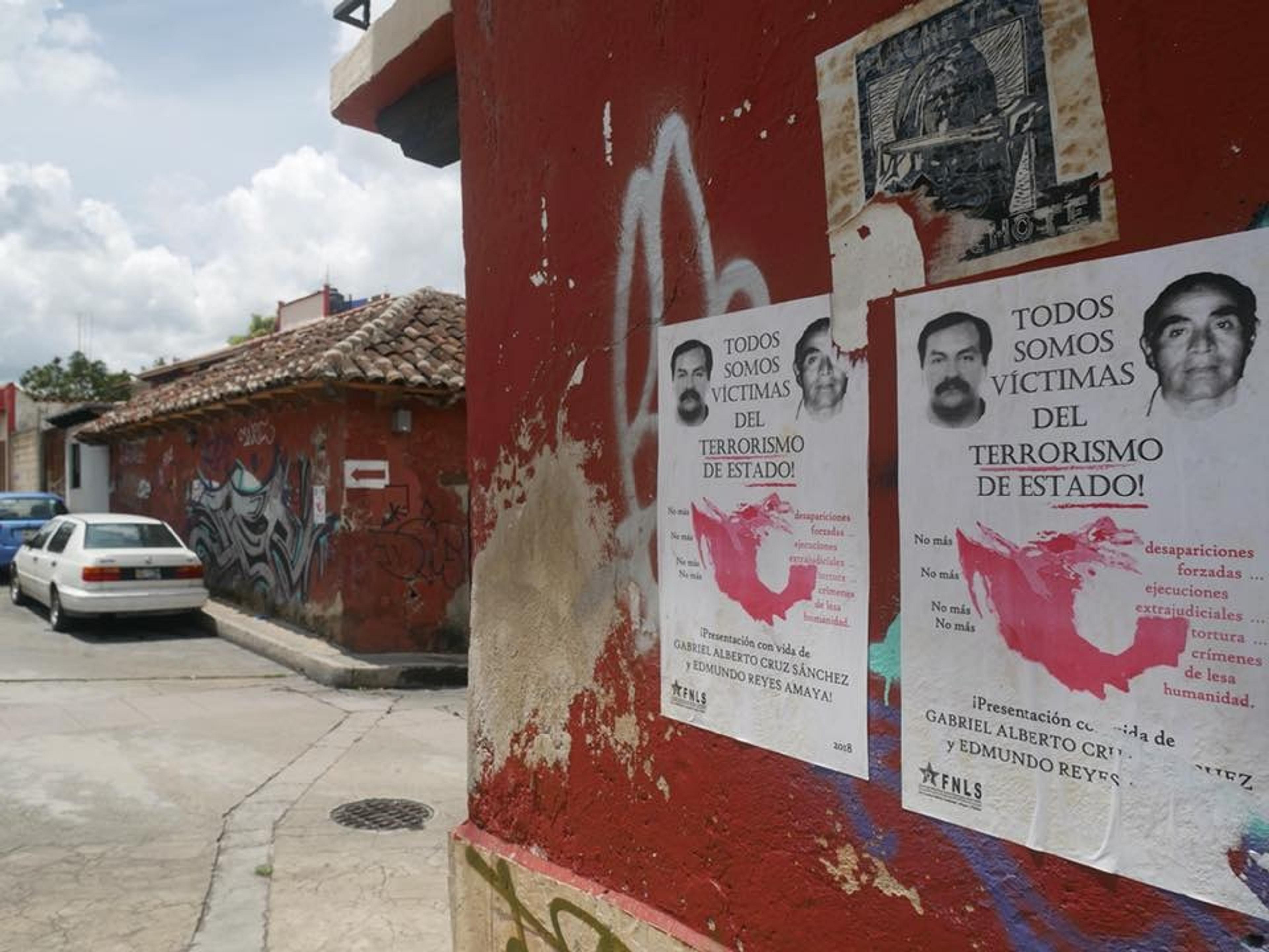 Posters advocating against state terrorism are pasted on a weathered red wall in a graffiti-decorated street in San Cristóbal de las Casas, Chiapas, Mexico.