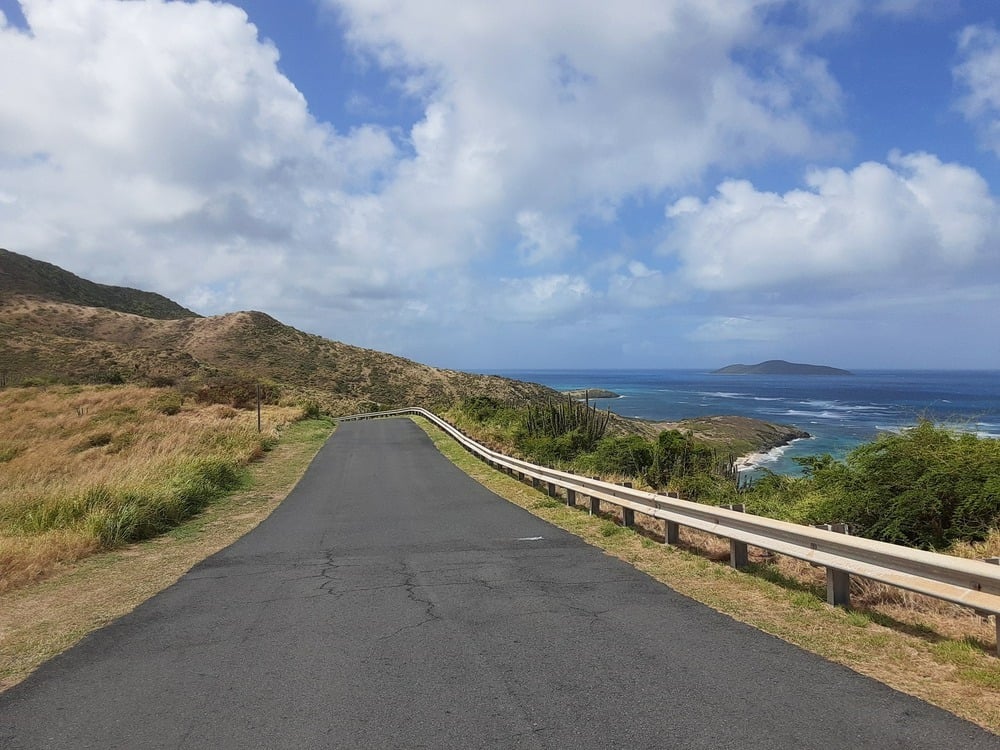 A coastal road curves alongside the scenic coastline of St. Croix in the U.S. Virgin Islands, with lush hills and the Caribbean Sea.