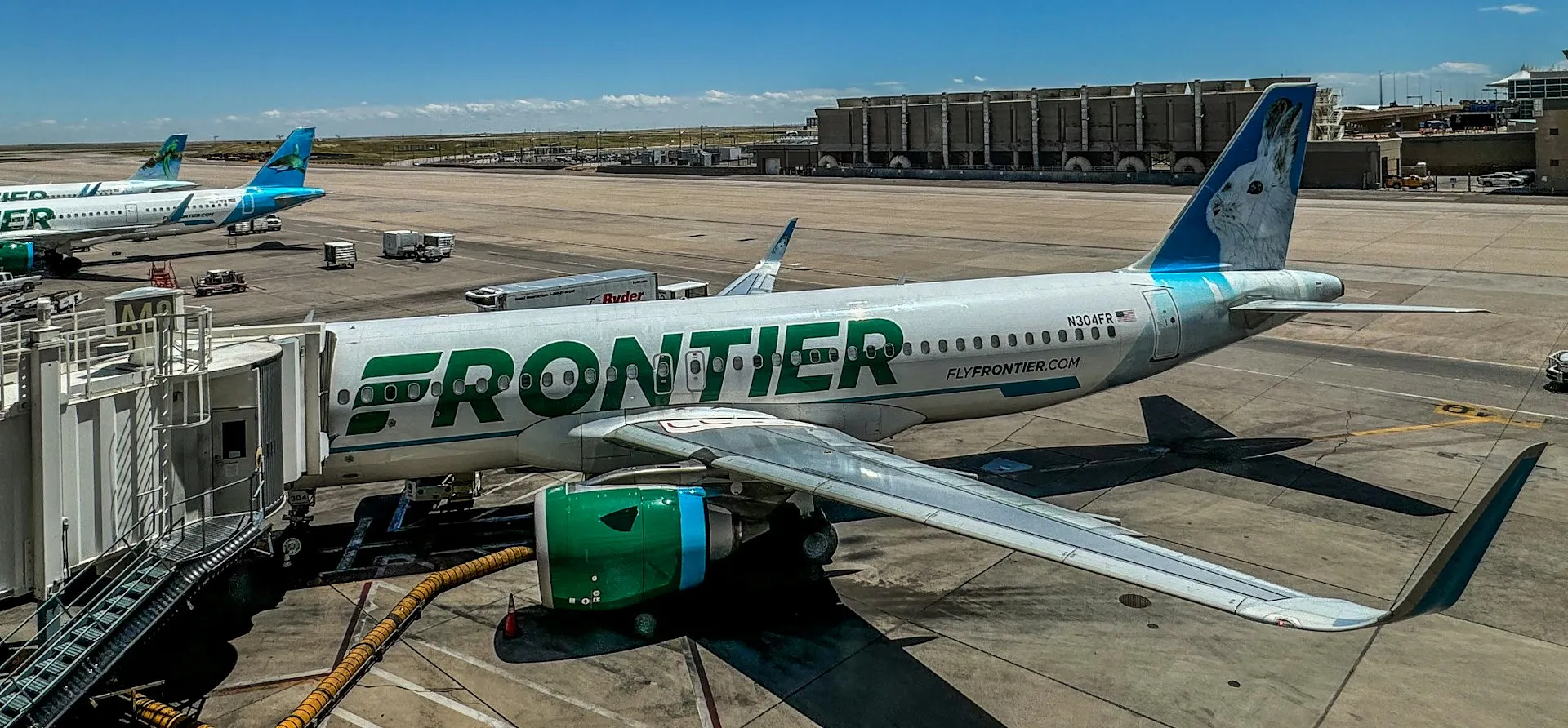 Frontier Airlines planes are parked at Denver International Airport under a blue sky with scattered clouds.
