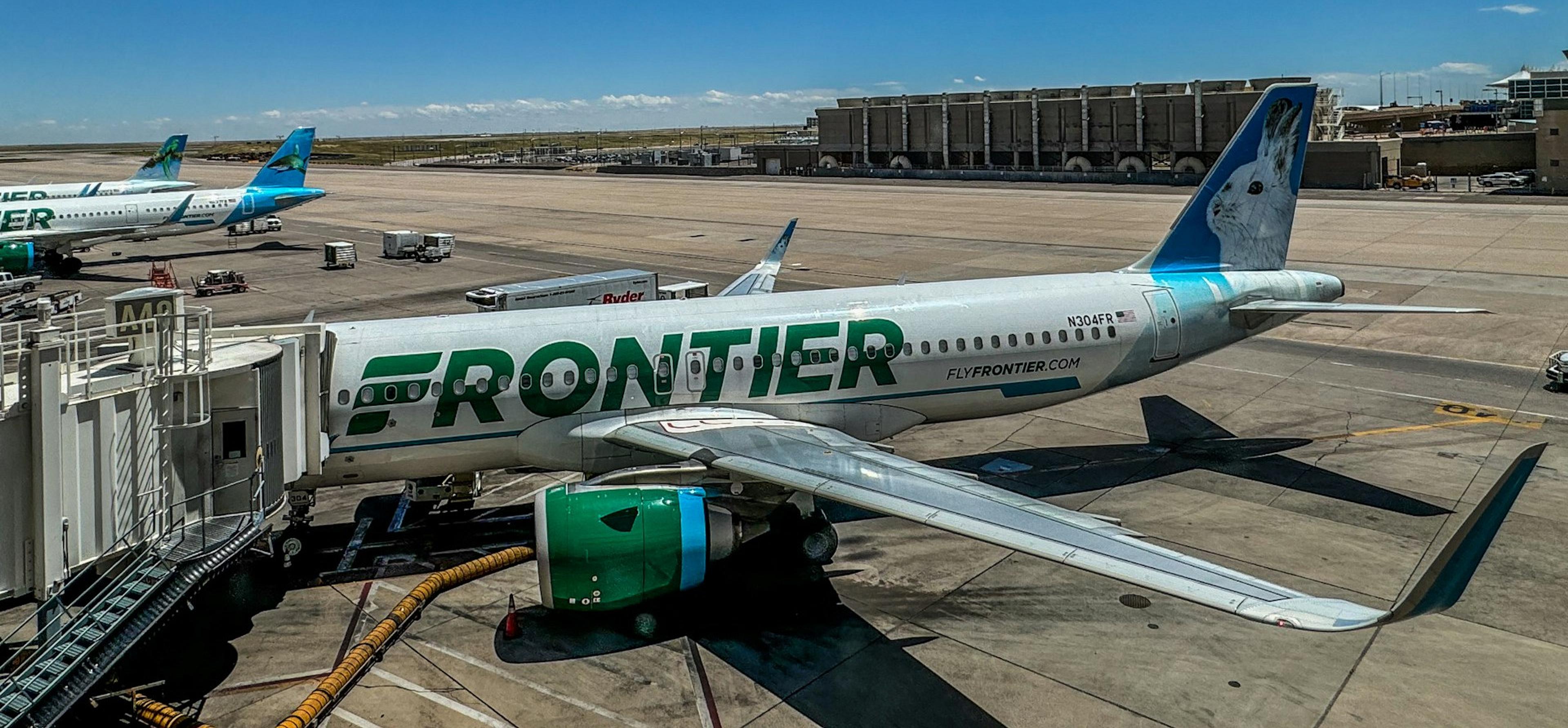Frontier Airlines planes are parked at Denver International Airport under a blue sky with scattered clouds.