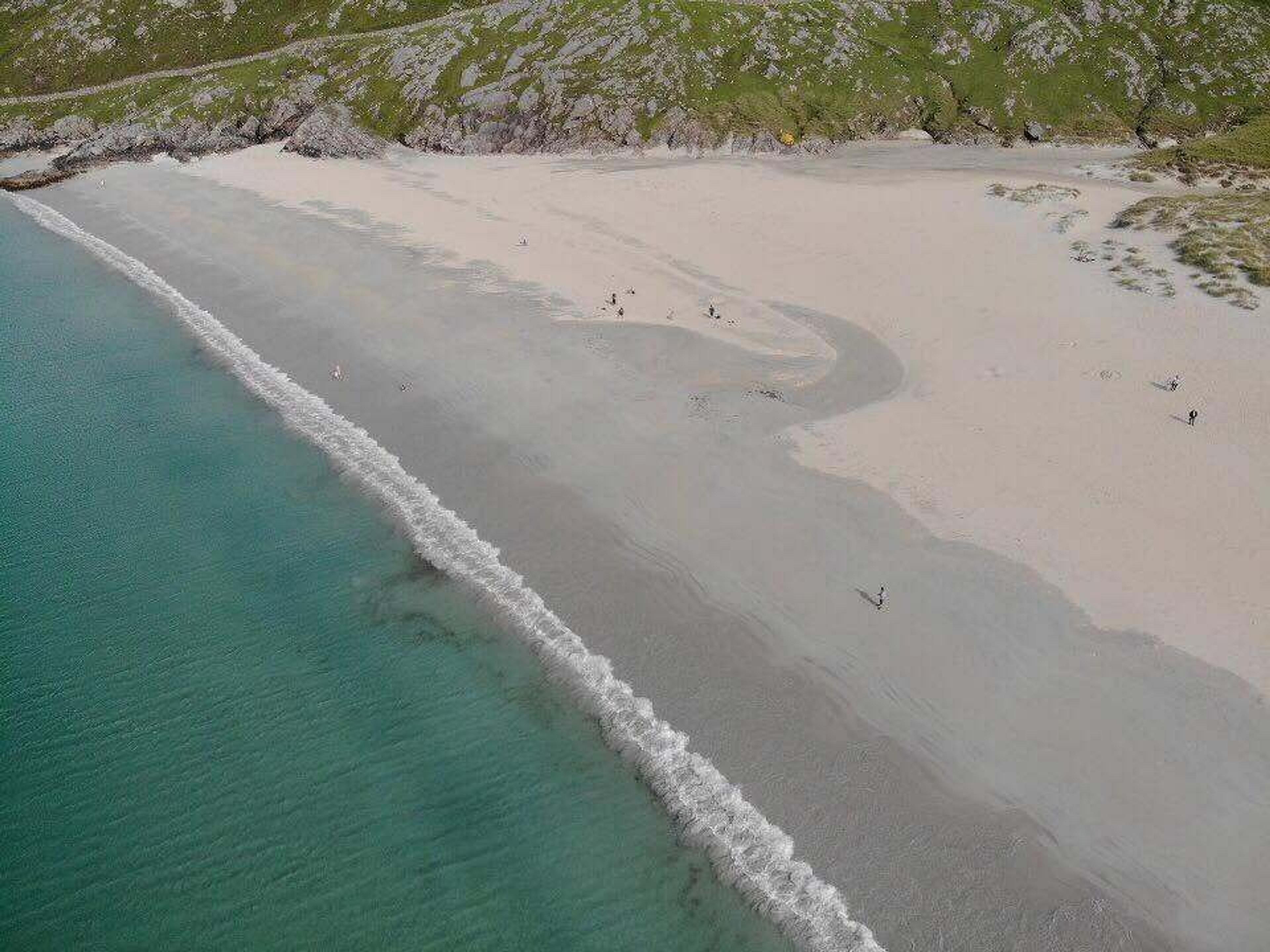 Turquoise waves gently lapping against the white sandy shore backed by rugged green hills in the Hebrides.