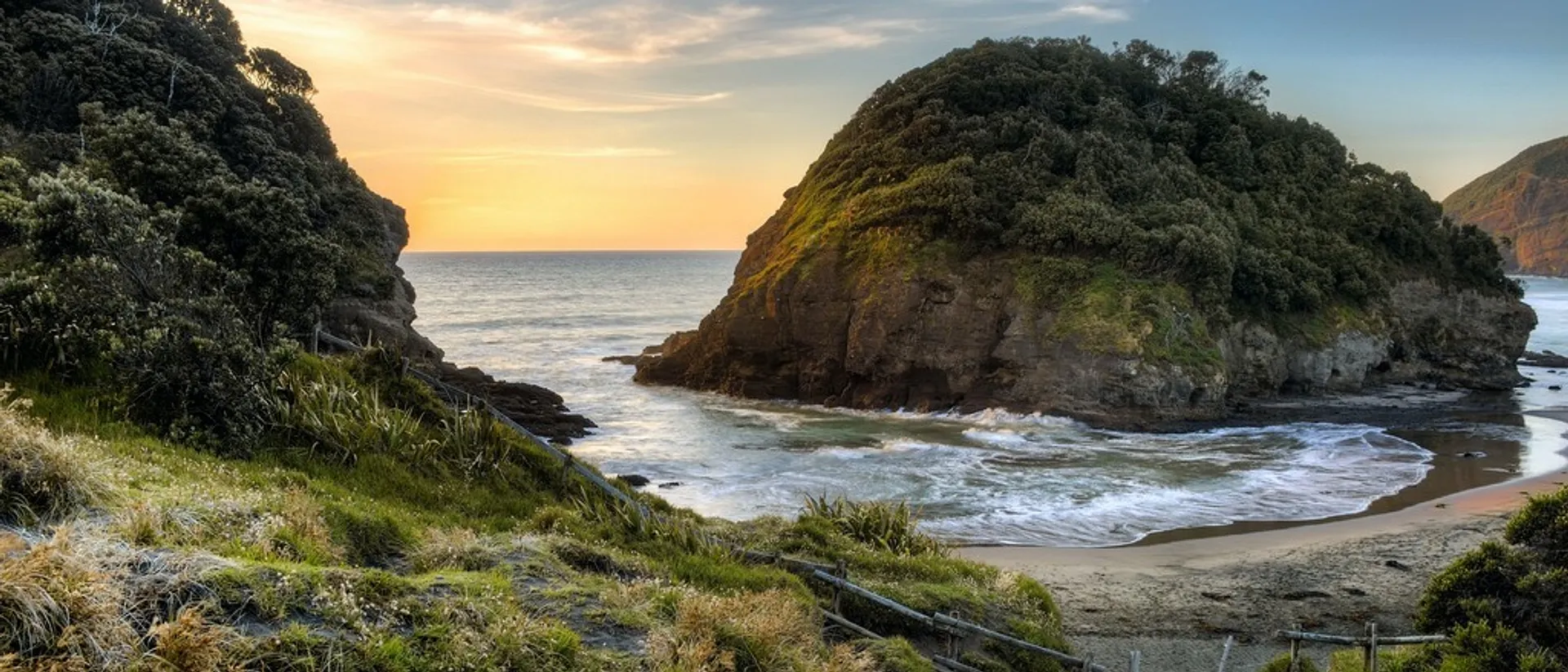 A stunning sunset view graces Whangarei Heads in New Zealand, featuring lush greenery and rugged cliffs.