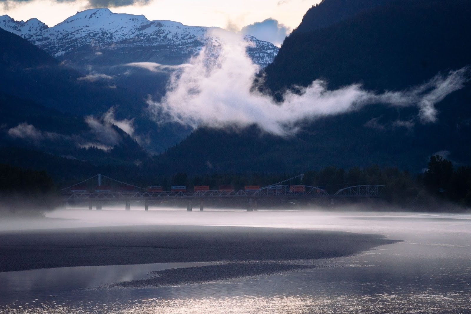 A misty view of the Fraser River with a bridge and train near Mount Robson in British Columbia, Canada.