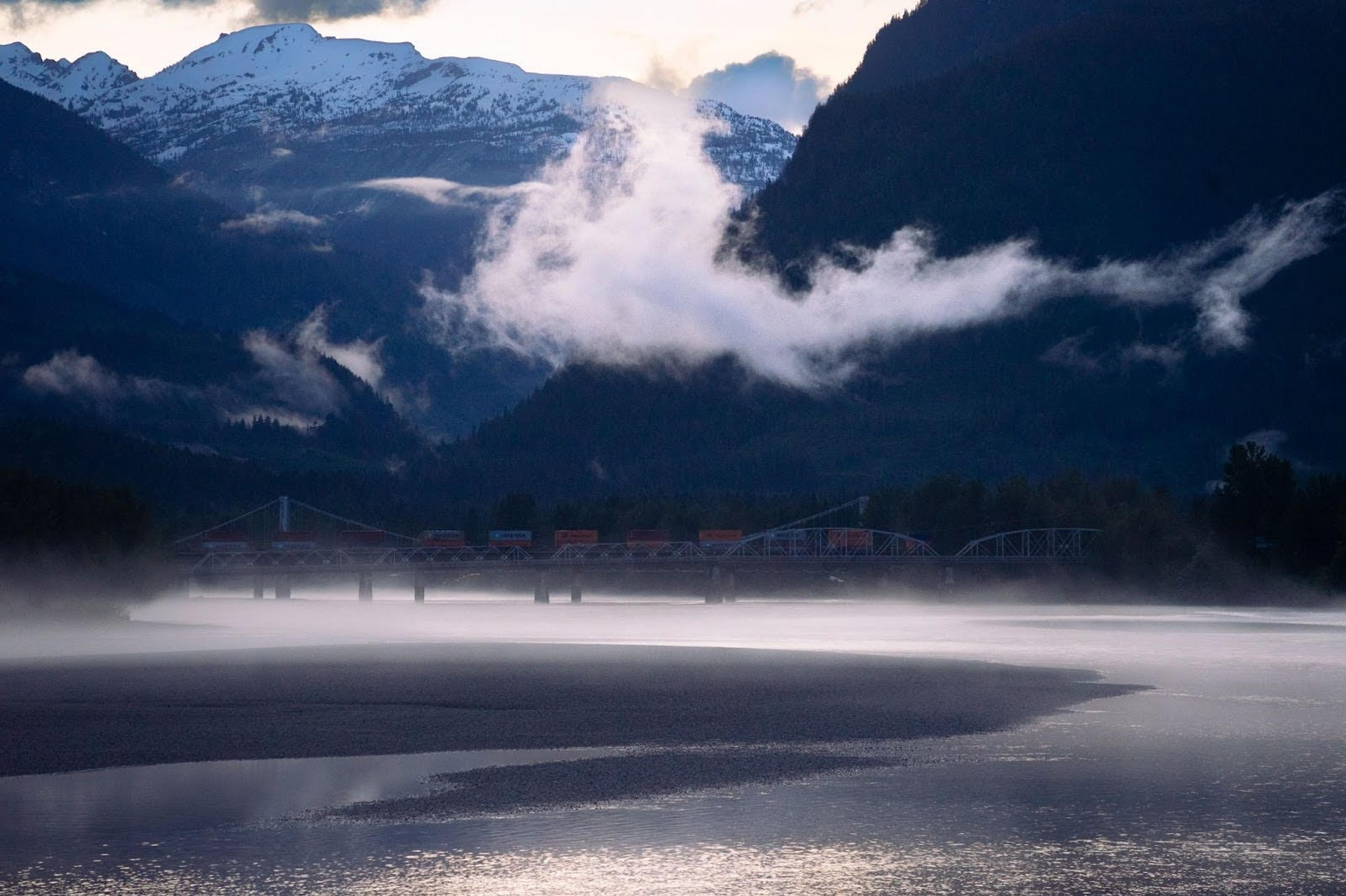 A misty view of the Fraser River with a bridge and train near Mount Robson in British Columbia, Canada.
