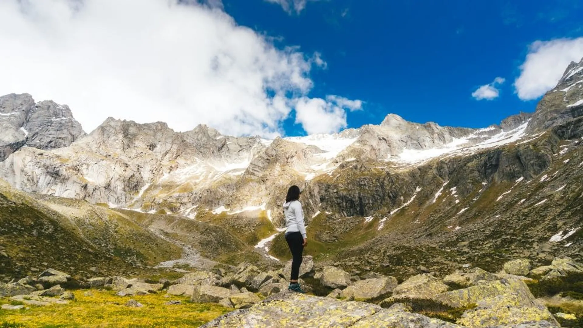 Person standing in a valley, looking up at snowy mountain tops
