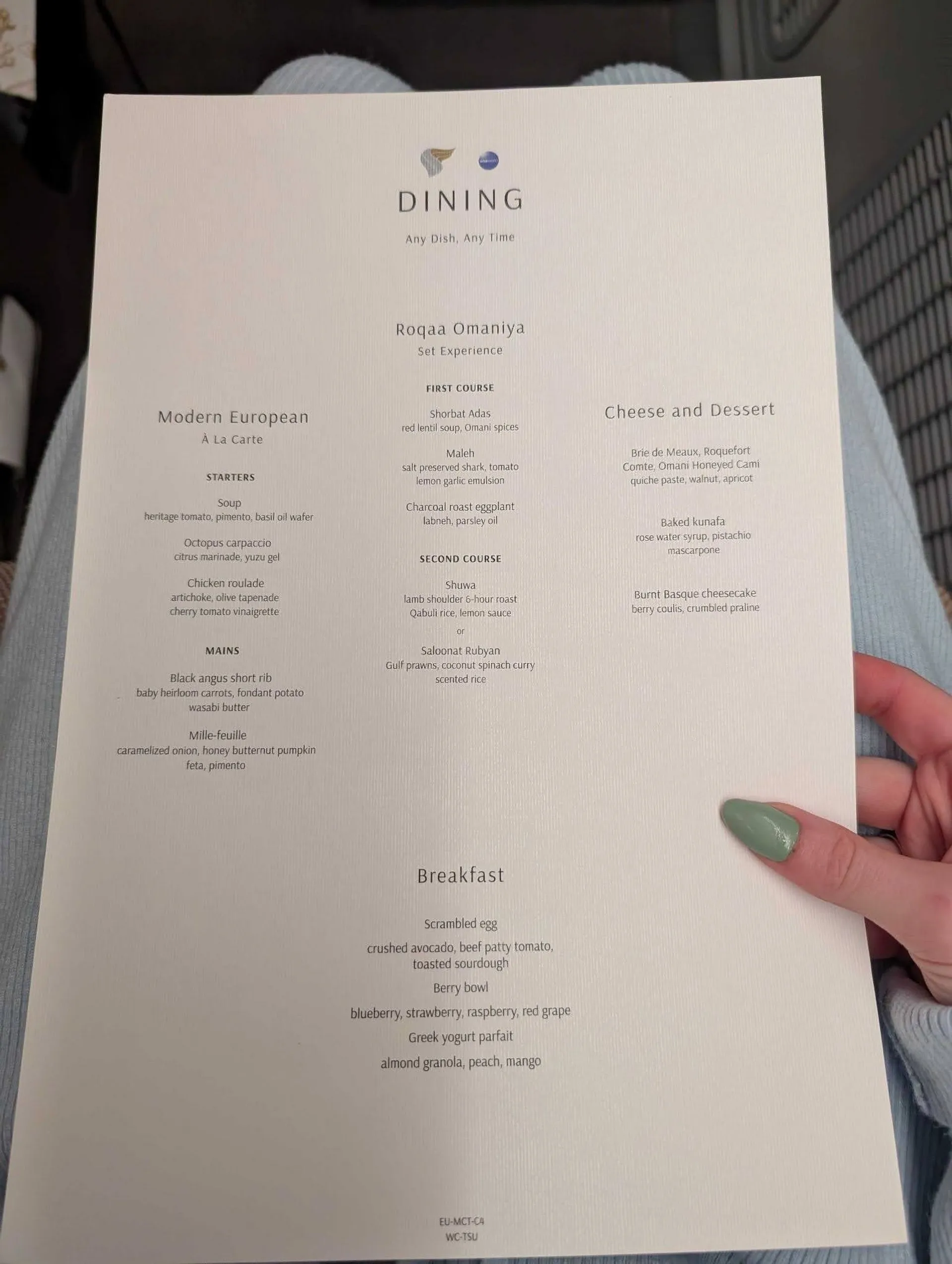 A dining menu from Oman Air featuring diverse culinary options is held on an airplane seat.