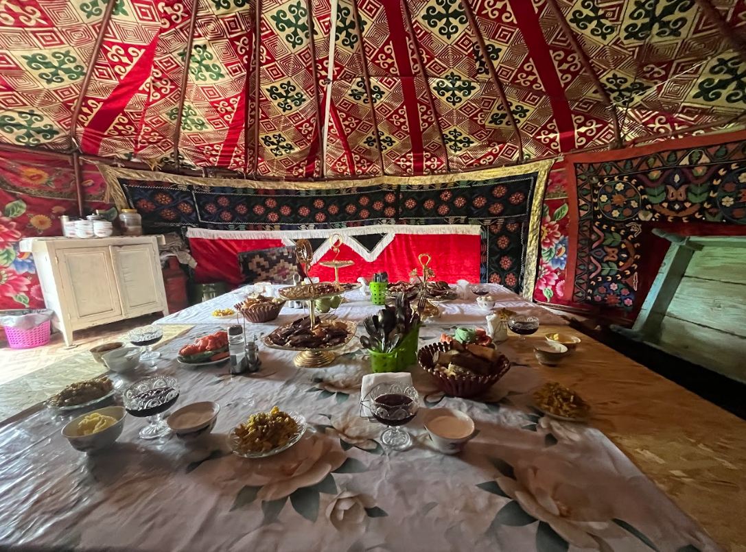 A richly decorated yurt interior in Central Asia features a table set with an array of traditional foods.