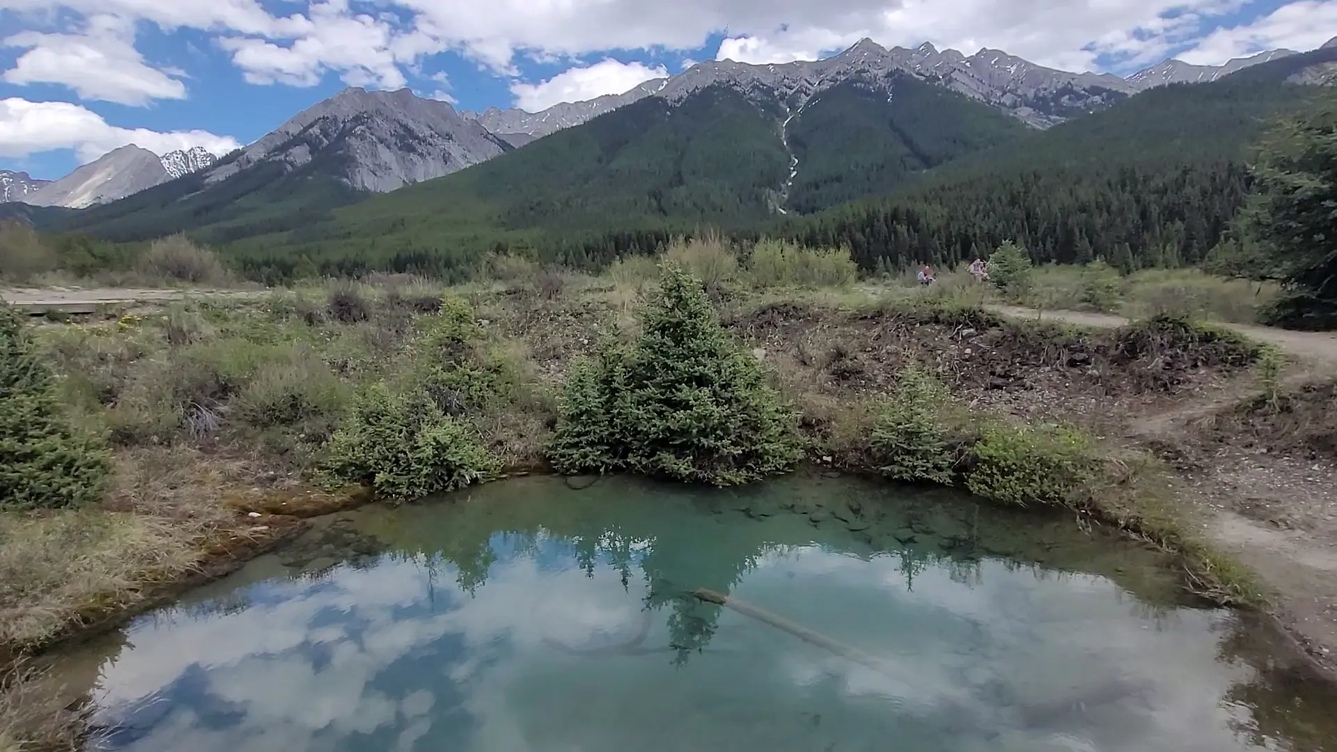 Turquoise Lake in the Canadian Rockies reflects the surrounding forest and snow-capped mountains under a partly cloudy sky.