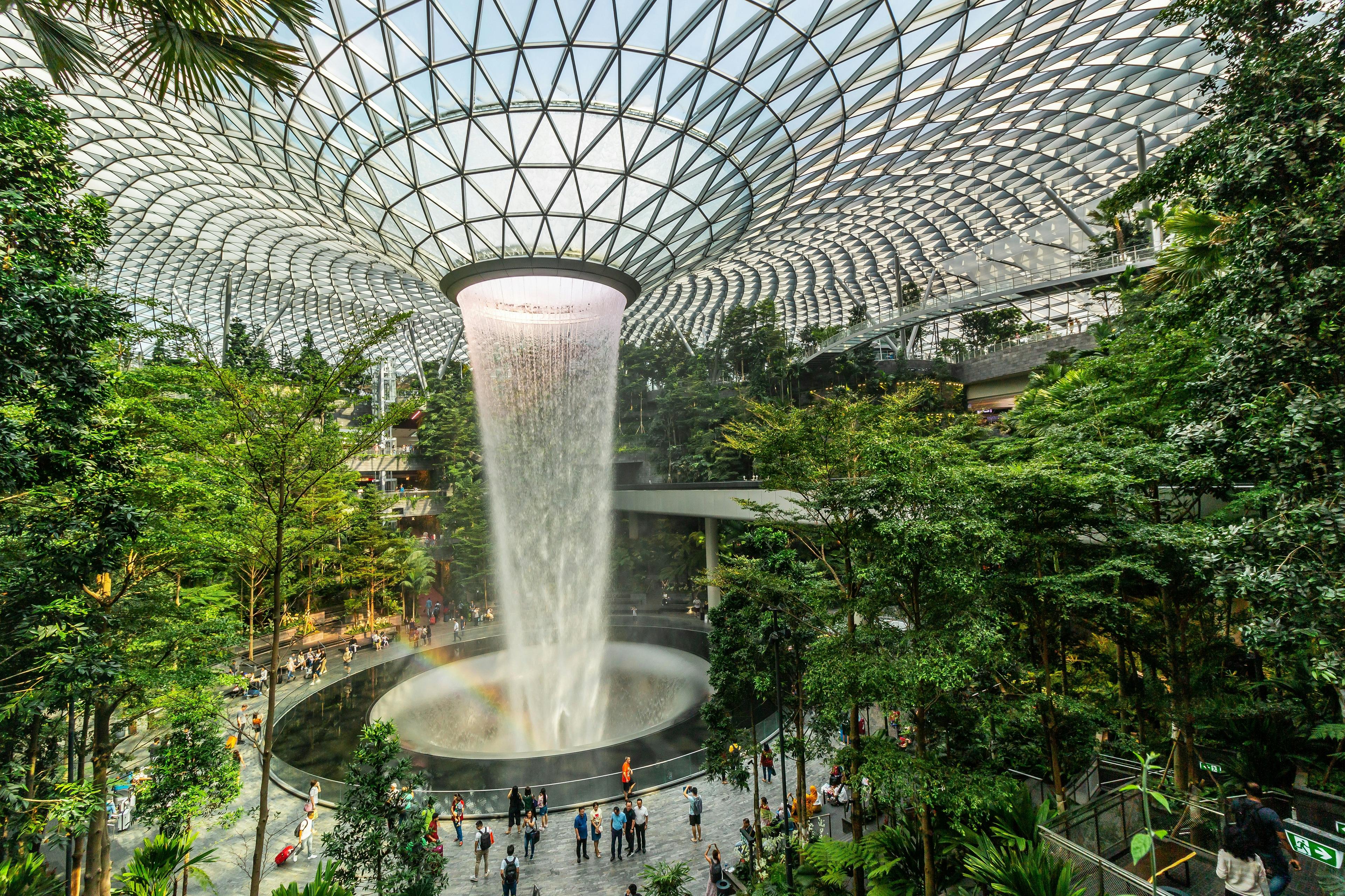 A stunning view of the indoor waterfall at Jewel Changi Airport in Singapore, surrounded by lush greenery under a futuristic glass dome.