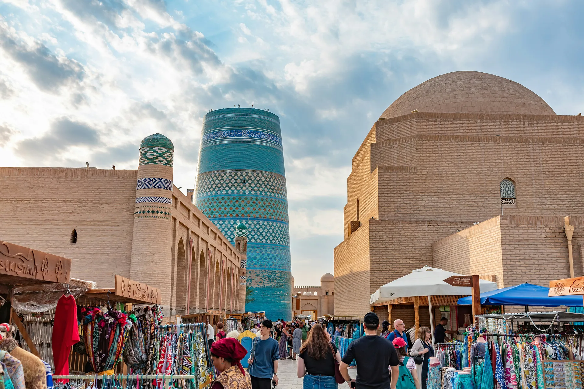 A bustling market scene unfolds in front of the iconic Kalta Minor Minaret in Khiva, Uzbekistan.