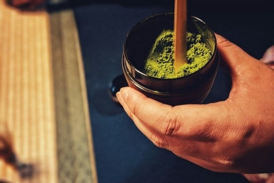 A hand prepares matcha tea in a traditional Japanese setting.