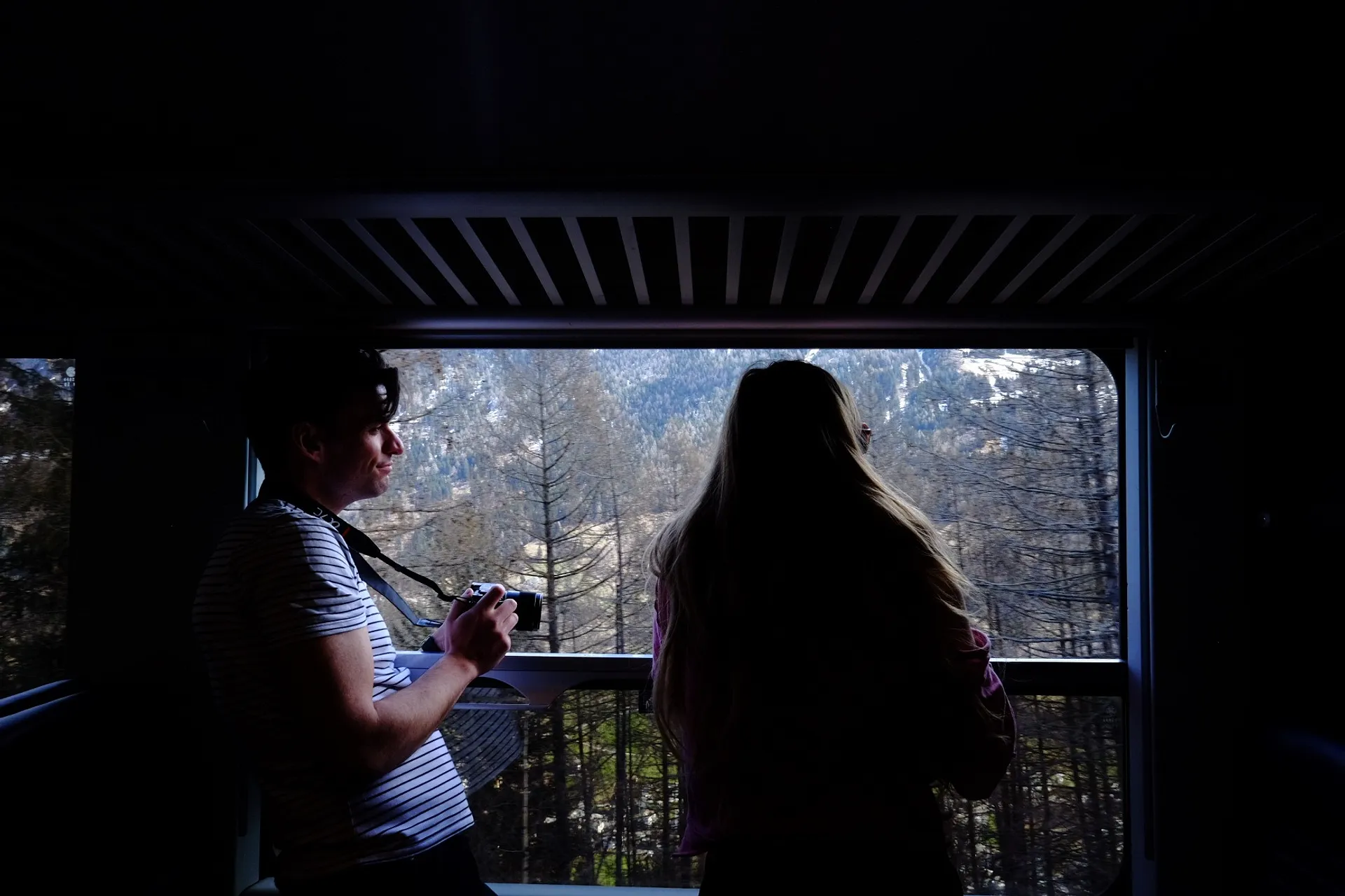 Two people enjoy the scenic mountain view through a train window, possibly somewhere in the Swiss Alps.