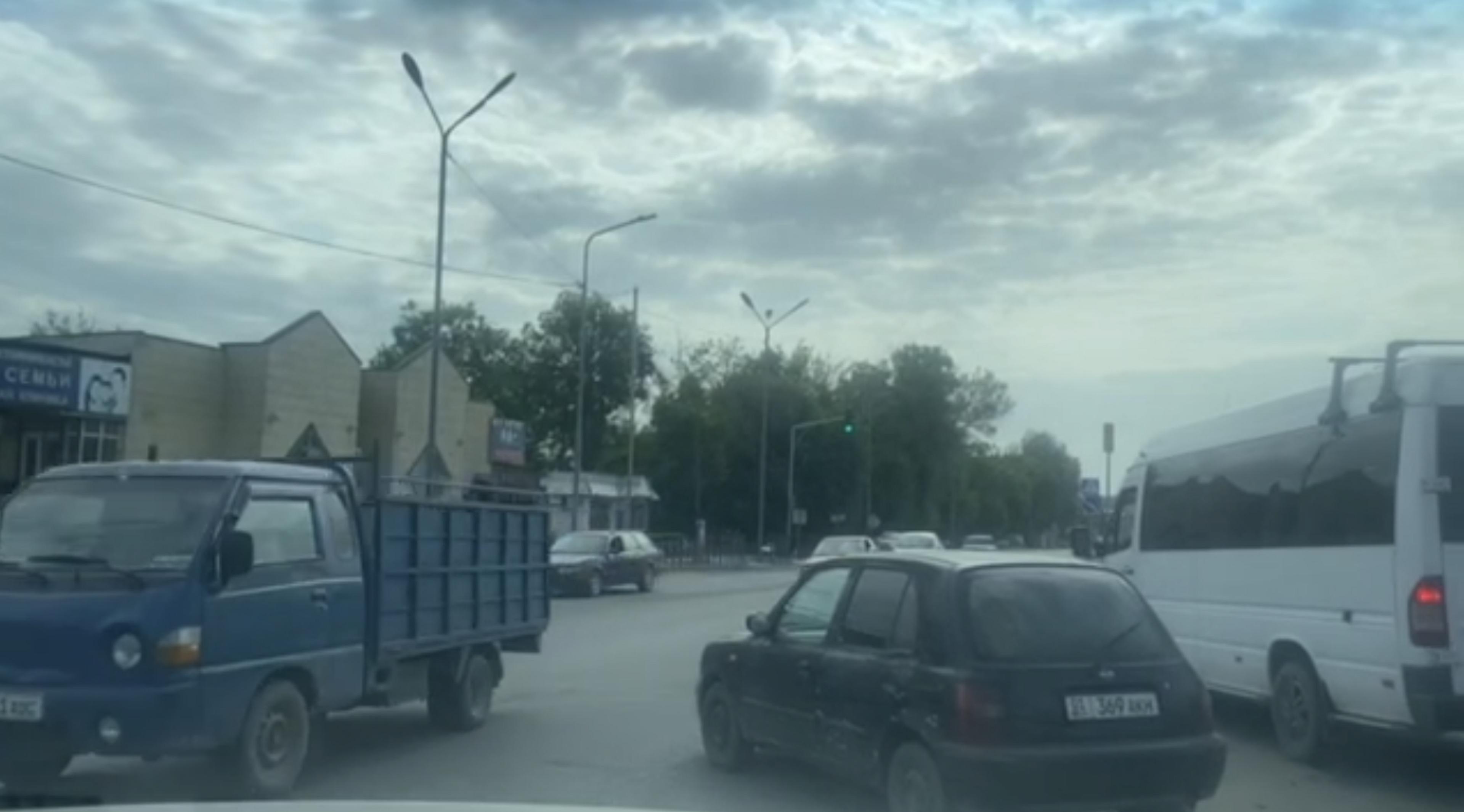 A busy intersection in Bishkek, Kyrgyzstan, with various vehicles and cloudy skies.