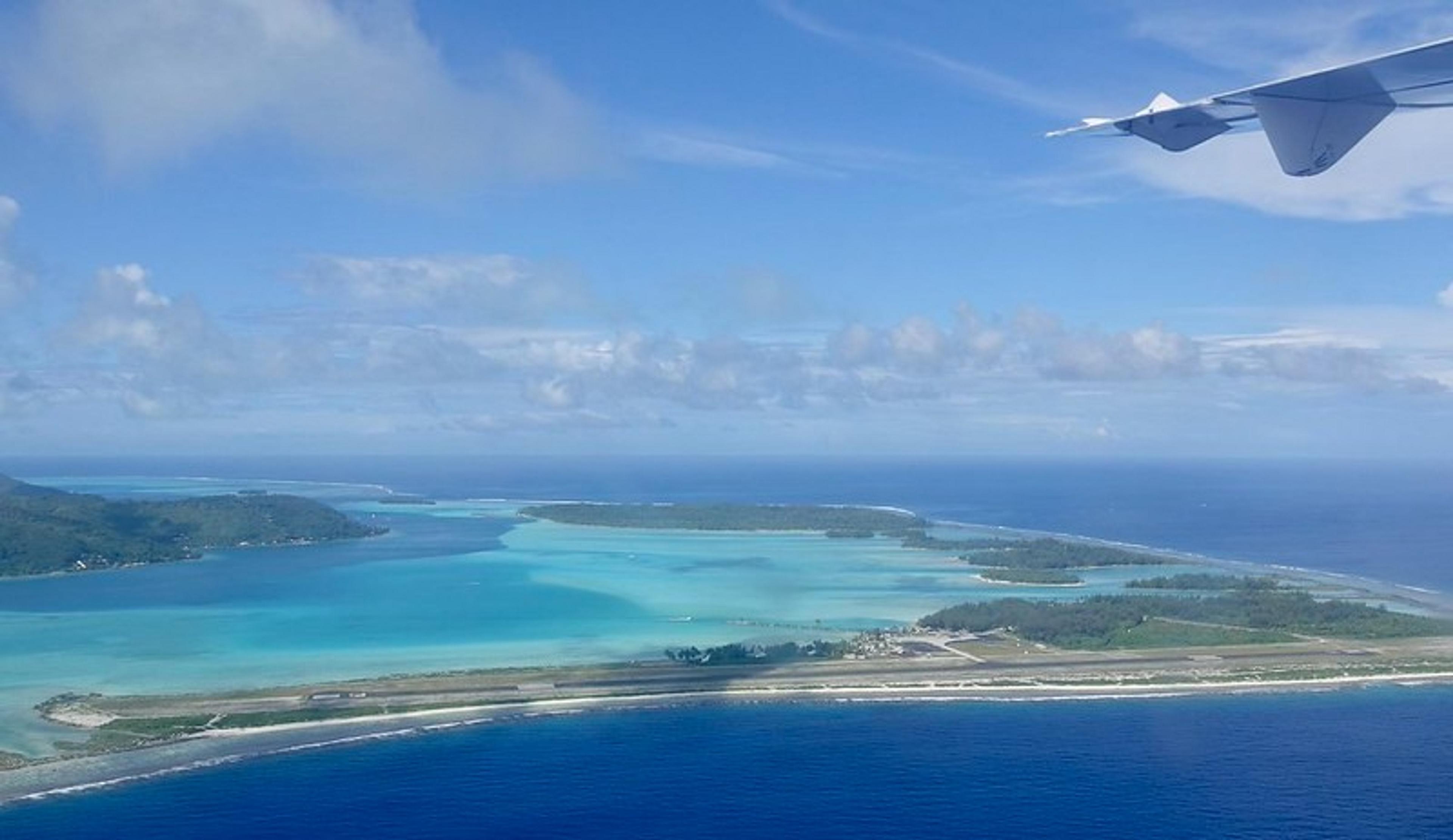 An aerial view of Bora Bora with turquoise waters and lush islands under the airplane wing.