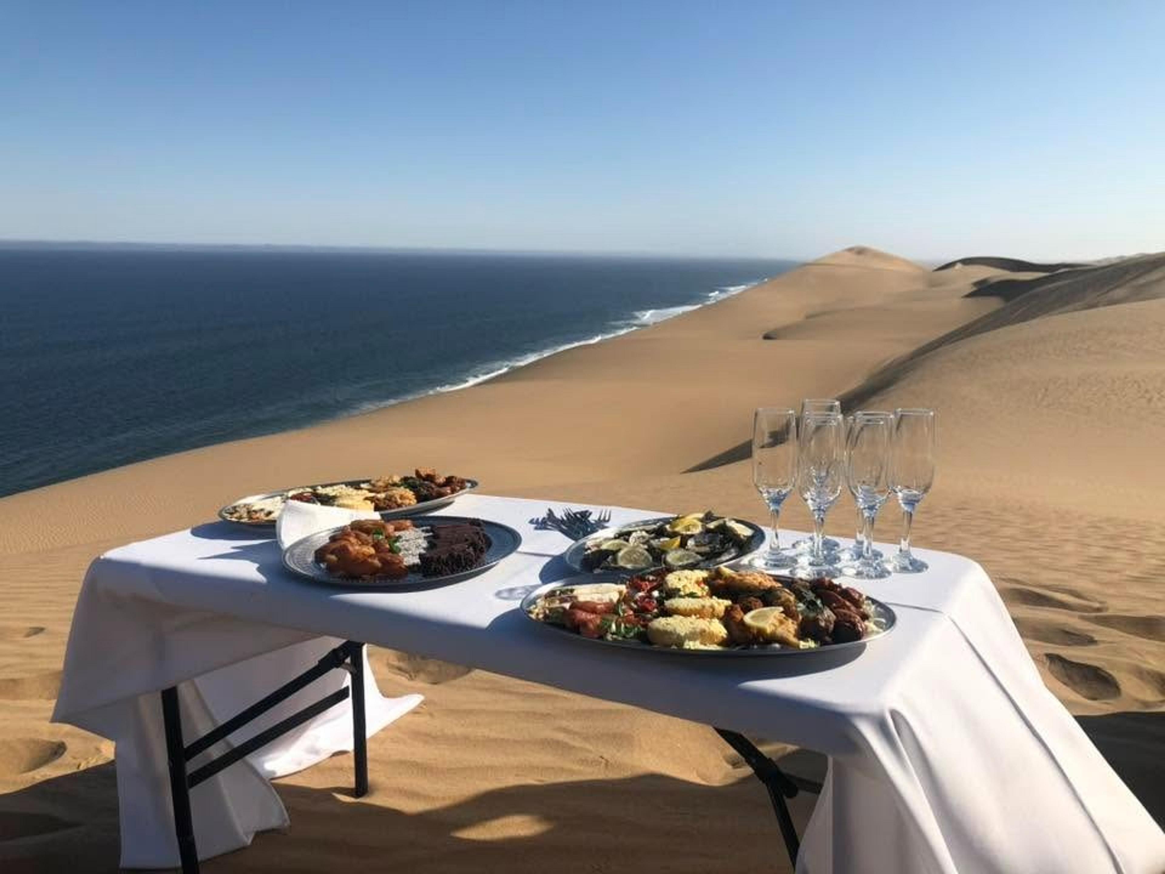 A luxurious picnic is set up on the sand dunes overlooking the Atlantic Ocean at Sandwich Harbour in Namibia.