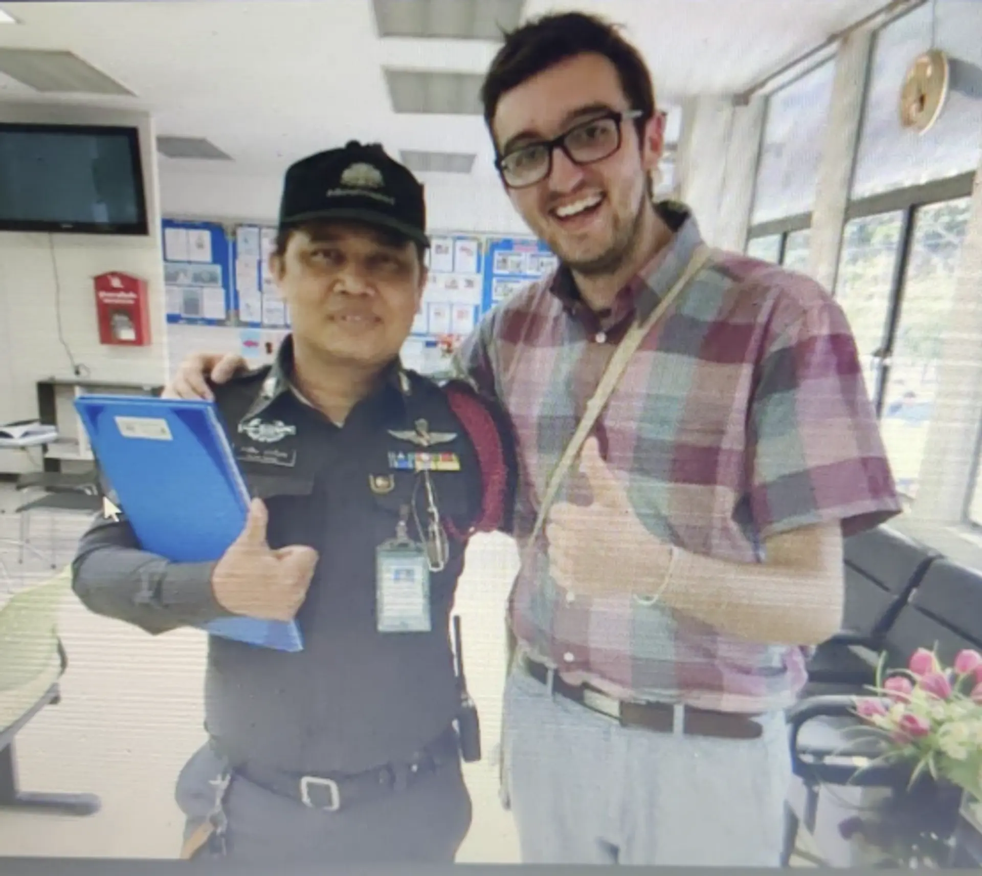 A person poses with a security officer inside a modern office or facility, possibly in an airport or governmental building.