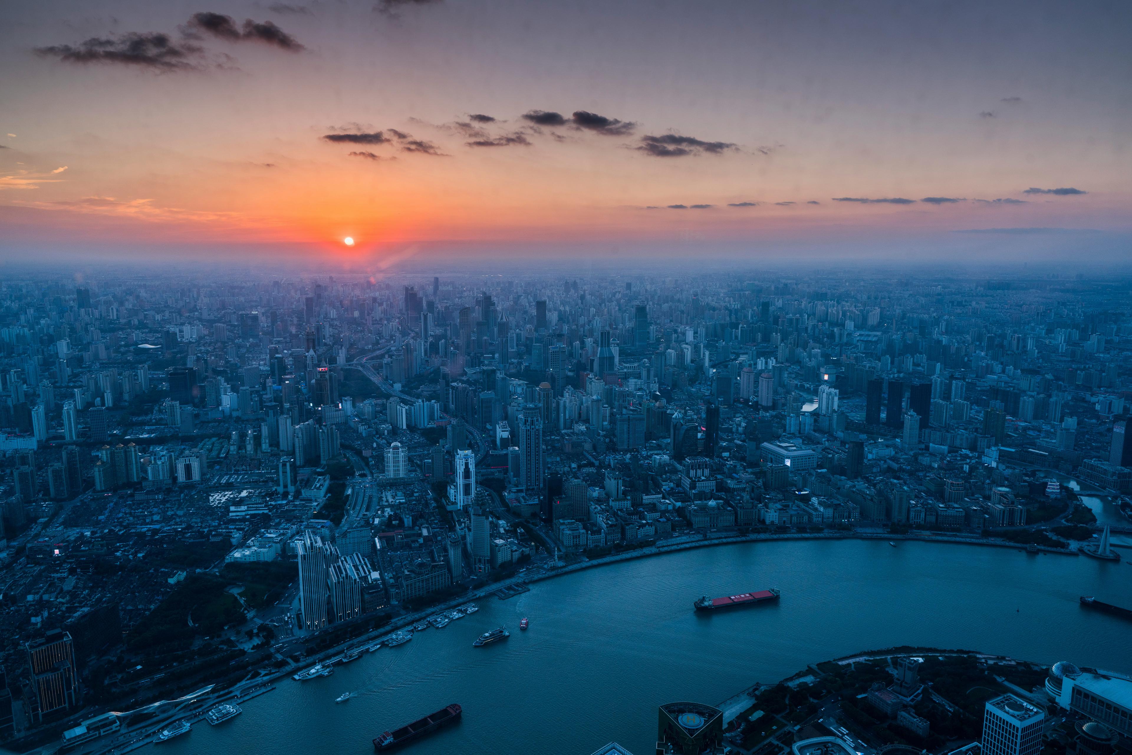 A stunning sunset casts a warm glow over the sprawling skyline of Shanghai, with the Huangpu River winding through the cityscape.