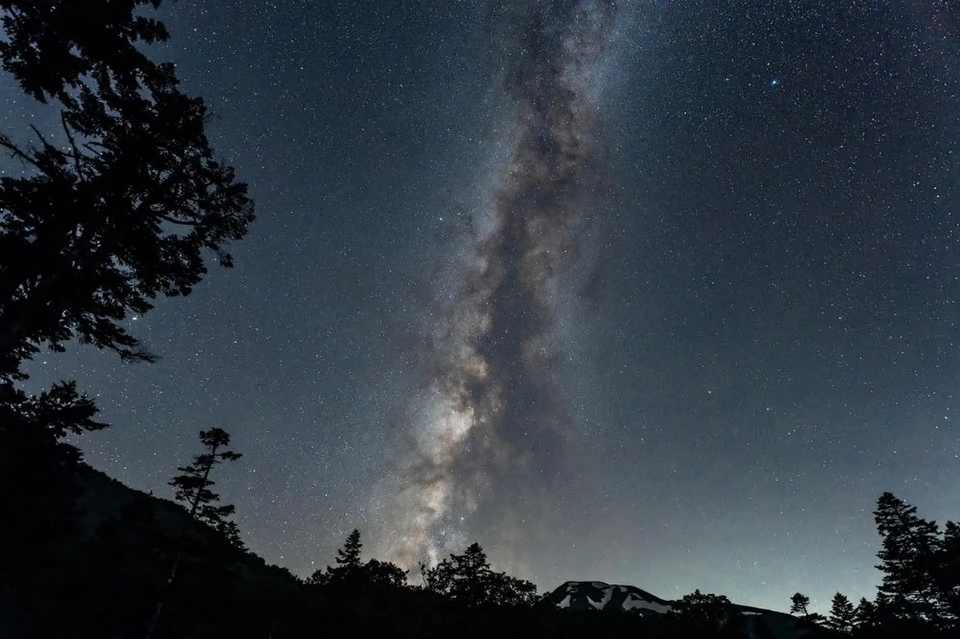 A breathtaking view of the Milky Way stretches across the night sky above the silhouetted peaks of Mt. Yotei, Japan.