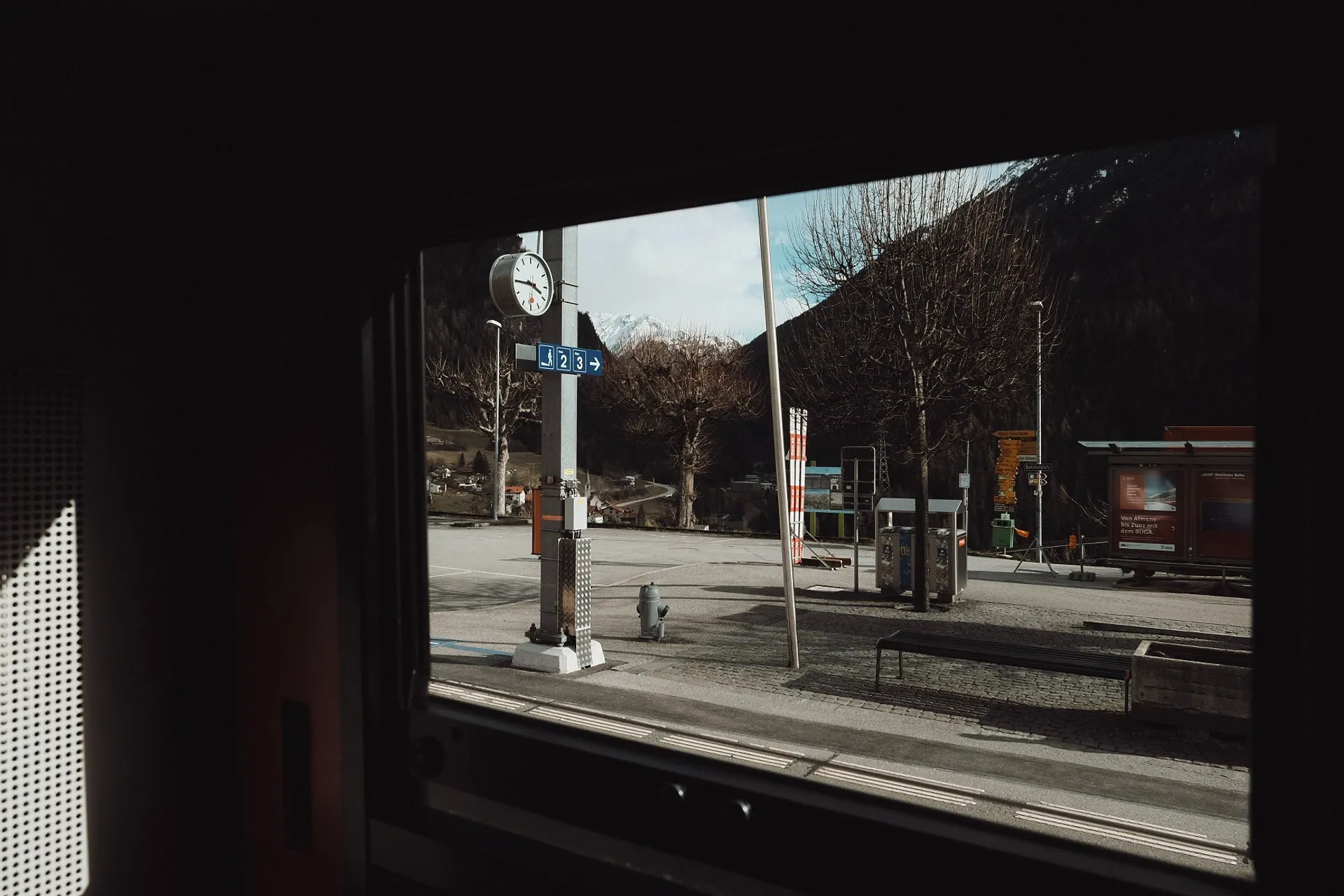 A glimpse of a quiet railway station platform in Filisur, Switzerland, framed by a train window.