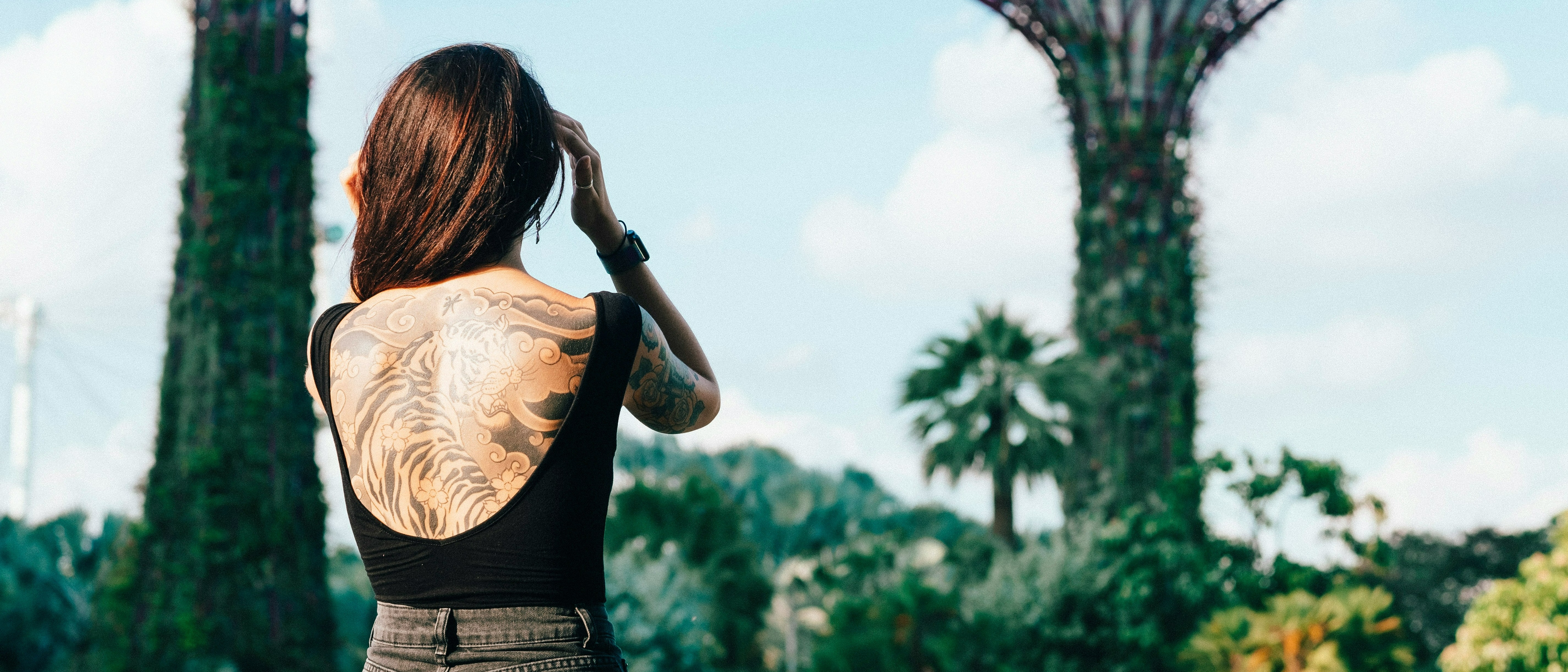 A woman with intricate tattoos stands in Singapore's Gardens by the Bay, with towering Supertrees in the background.