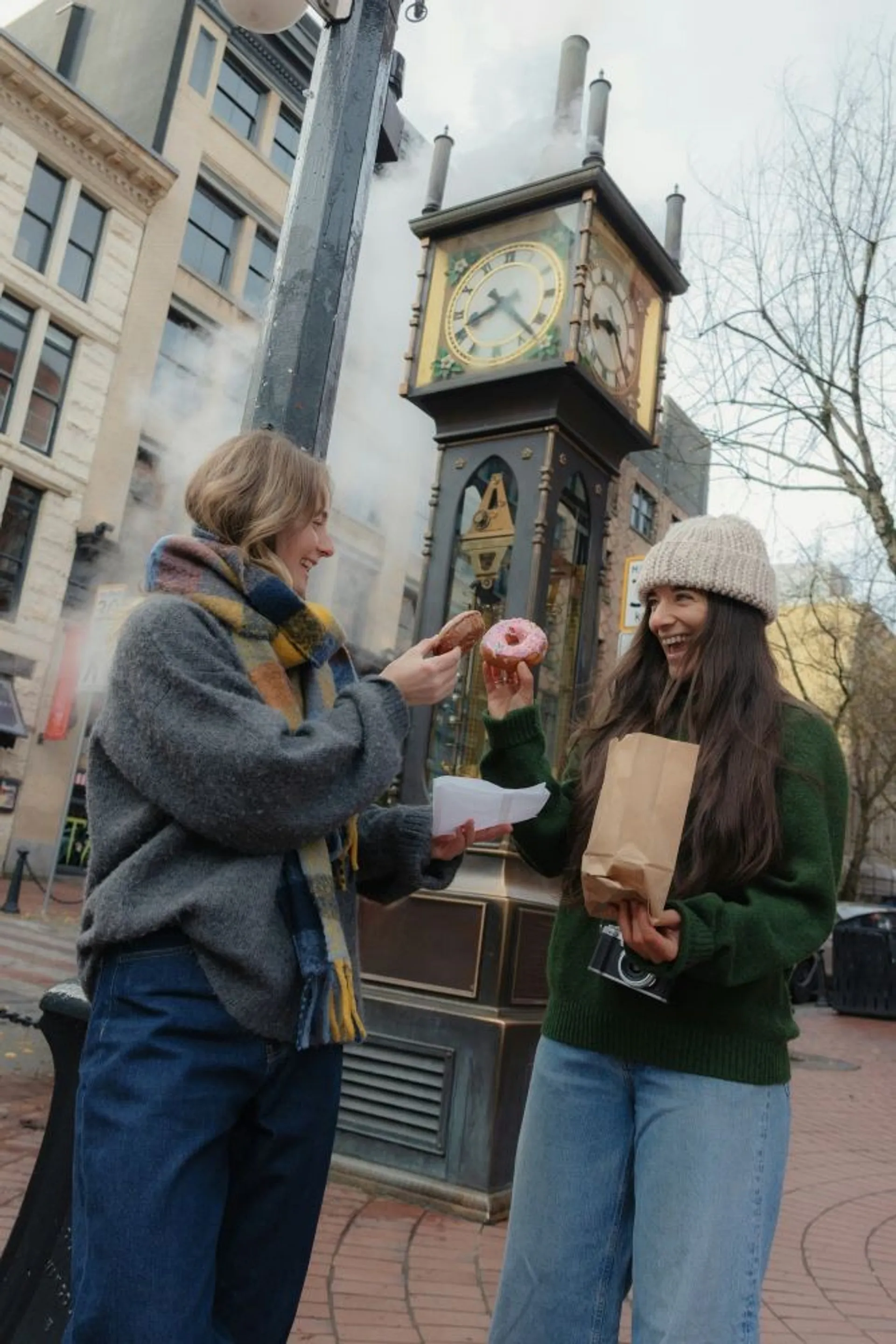 Two people enjoy pastries in front of the iconic steam clock in Vancouver's Gastown district.