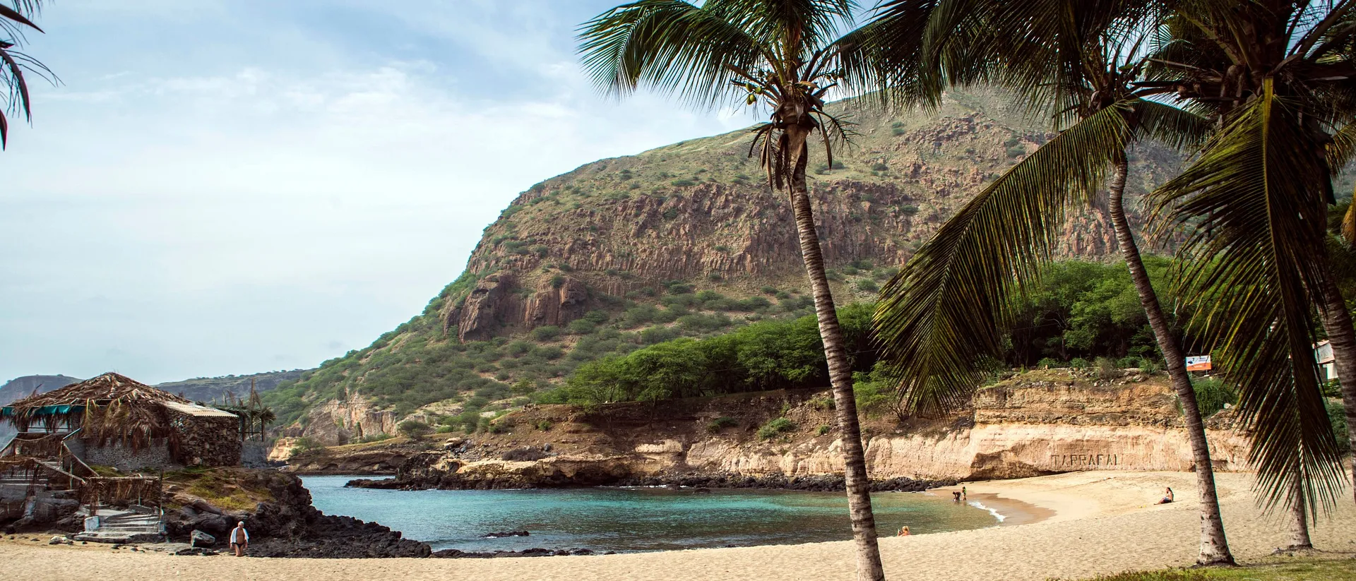 A serene coastal scene at Praia de Tarrafal in Cape Verde, framed by palm trees and rocky cliffs.