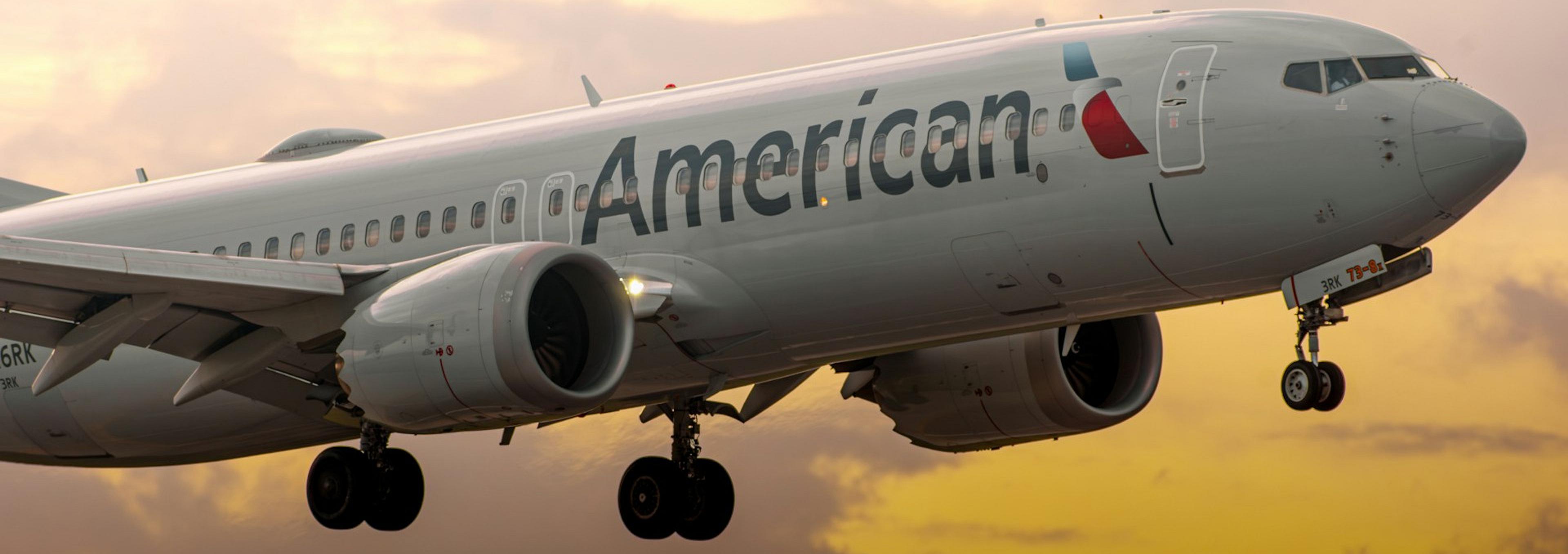 An American Airlines plane approaches for landing against a dramatic sunset sky.
