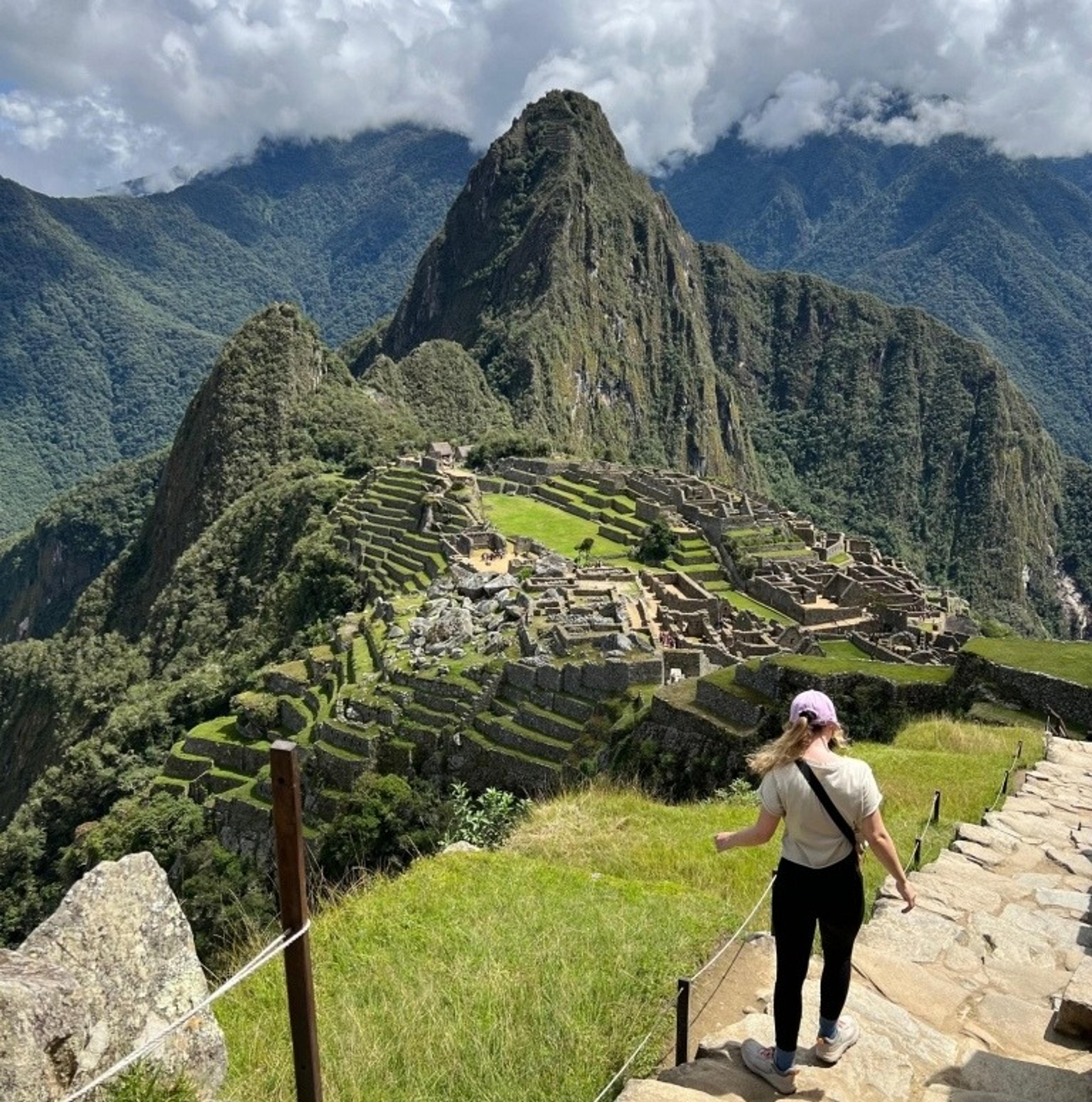 Flight Finder Lauren descends a stone path overlooking the ancient Incan citadel of Machu Picchu, surrounded by lush mountains.