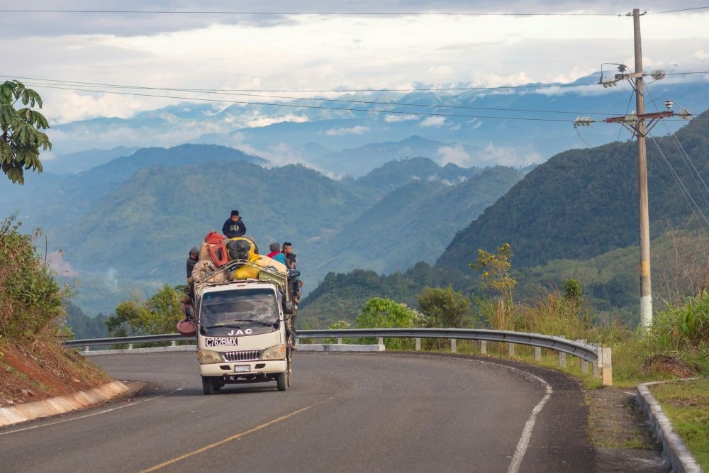 A truck laden with passengers and cargo navigates a winding road in the lush, mountainous region of Oaxaca, Mexico.