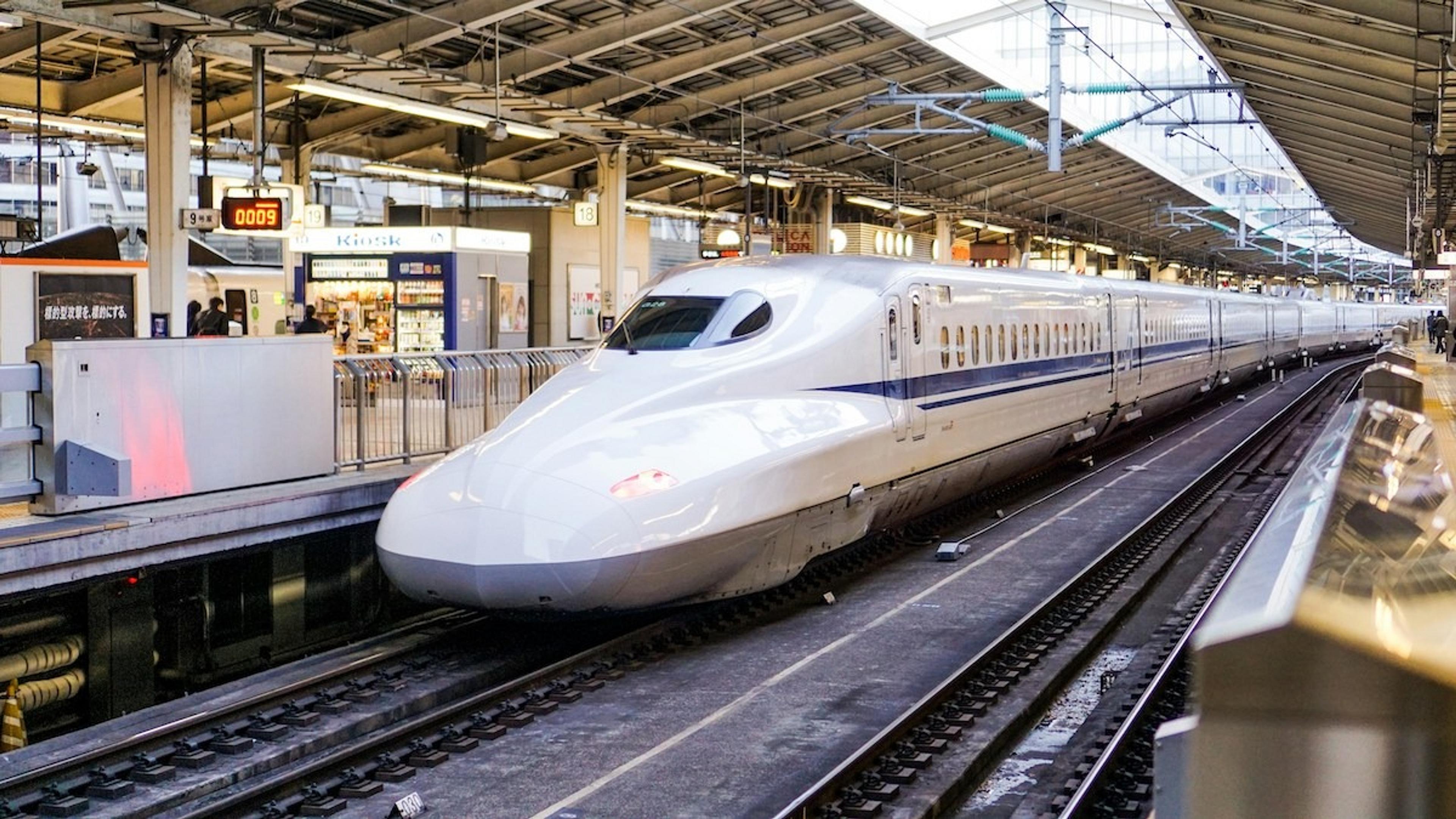 A sleek Shinkansen train waits at Tokyo Station, showcasing Japan's iconic bullet train design against the station's modern architecture.