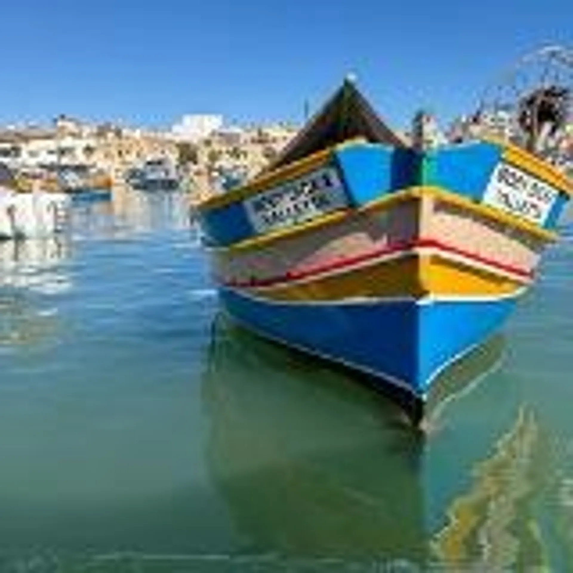 A traditional Maltese luzzu boat floats peacefully in the vibrant waters of Marsaxlokk Harbour.