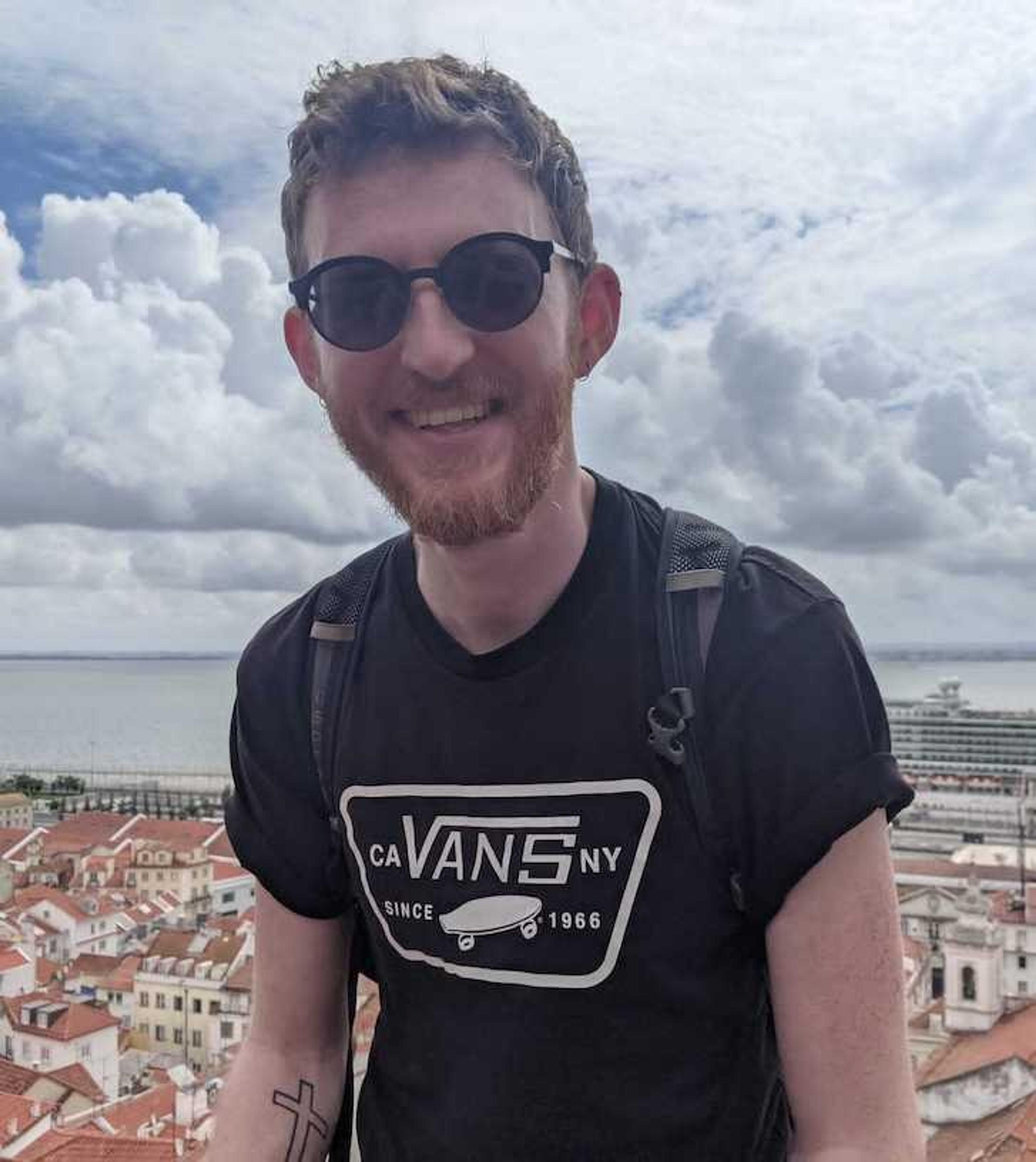 A person standing with a view of Lisbon's red-roofed buildings and a river in the background.
