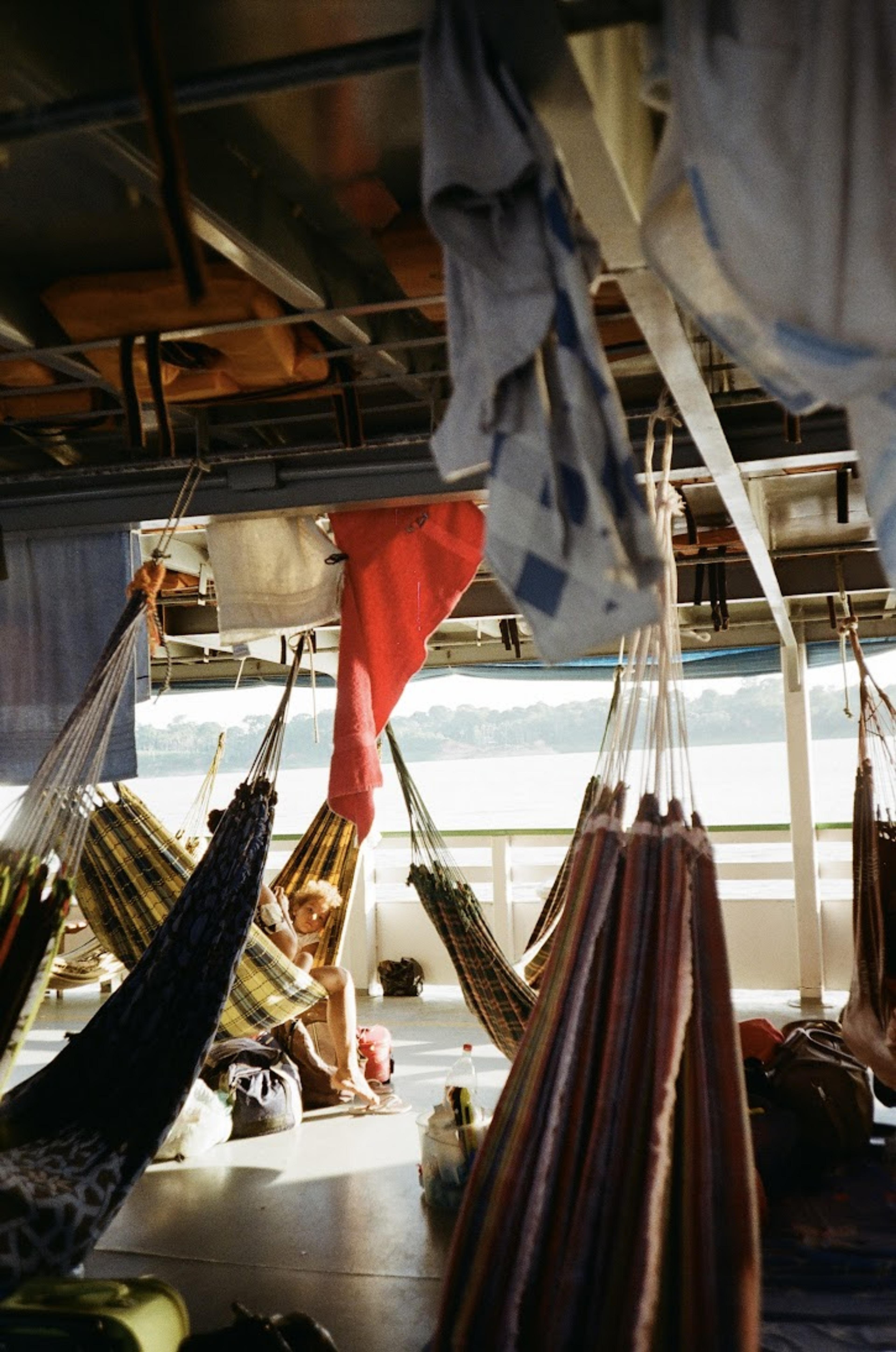 Hammocks hang under a canopy on a boat traveling along the Amazon River.