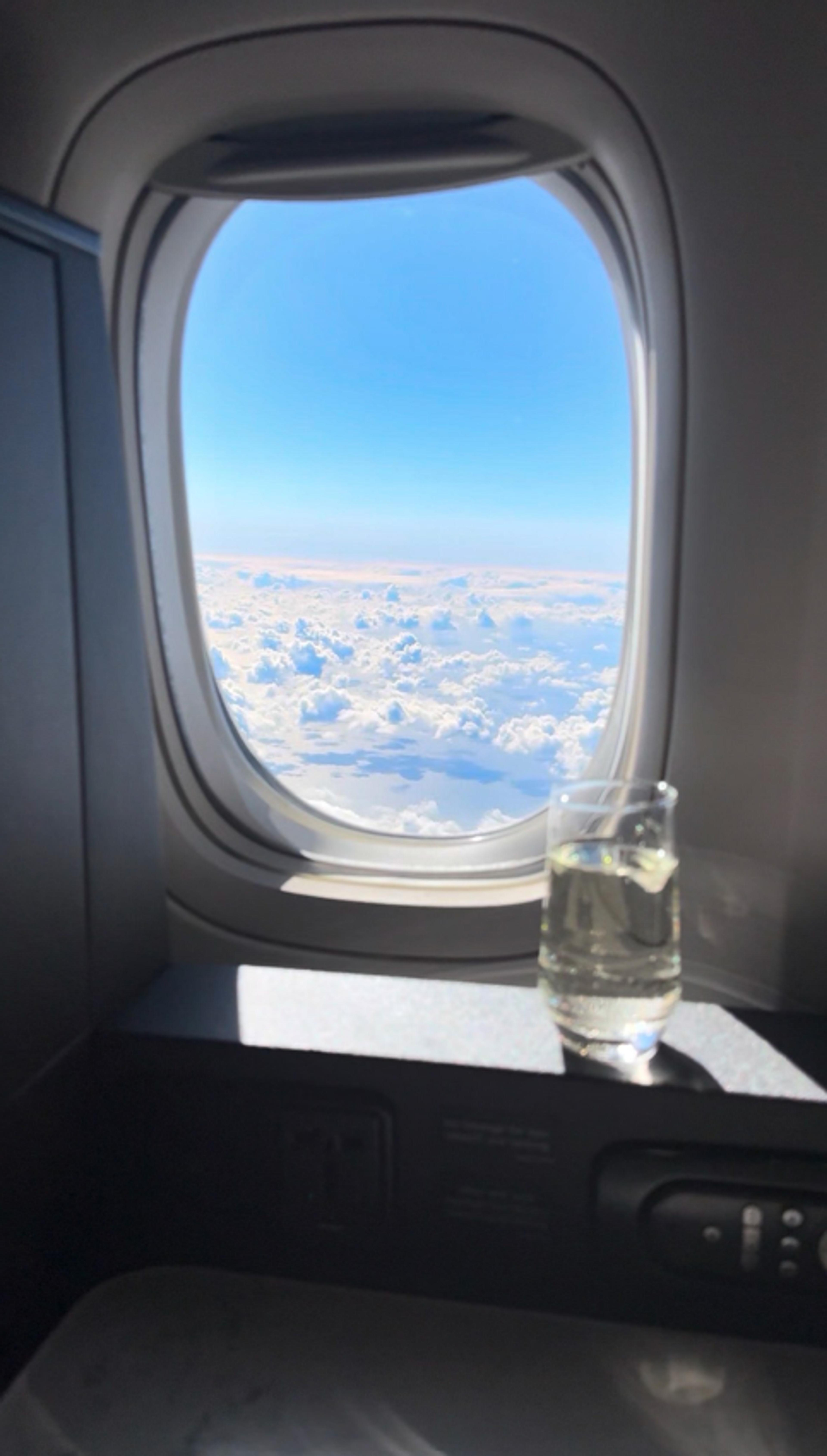 A view of fluffy white clouds from an airplane window with a glass of water on the ledge.